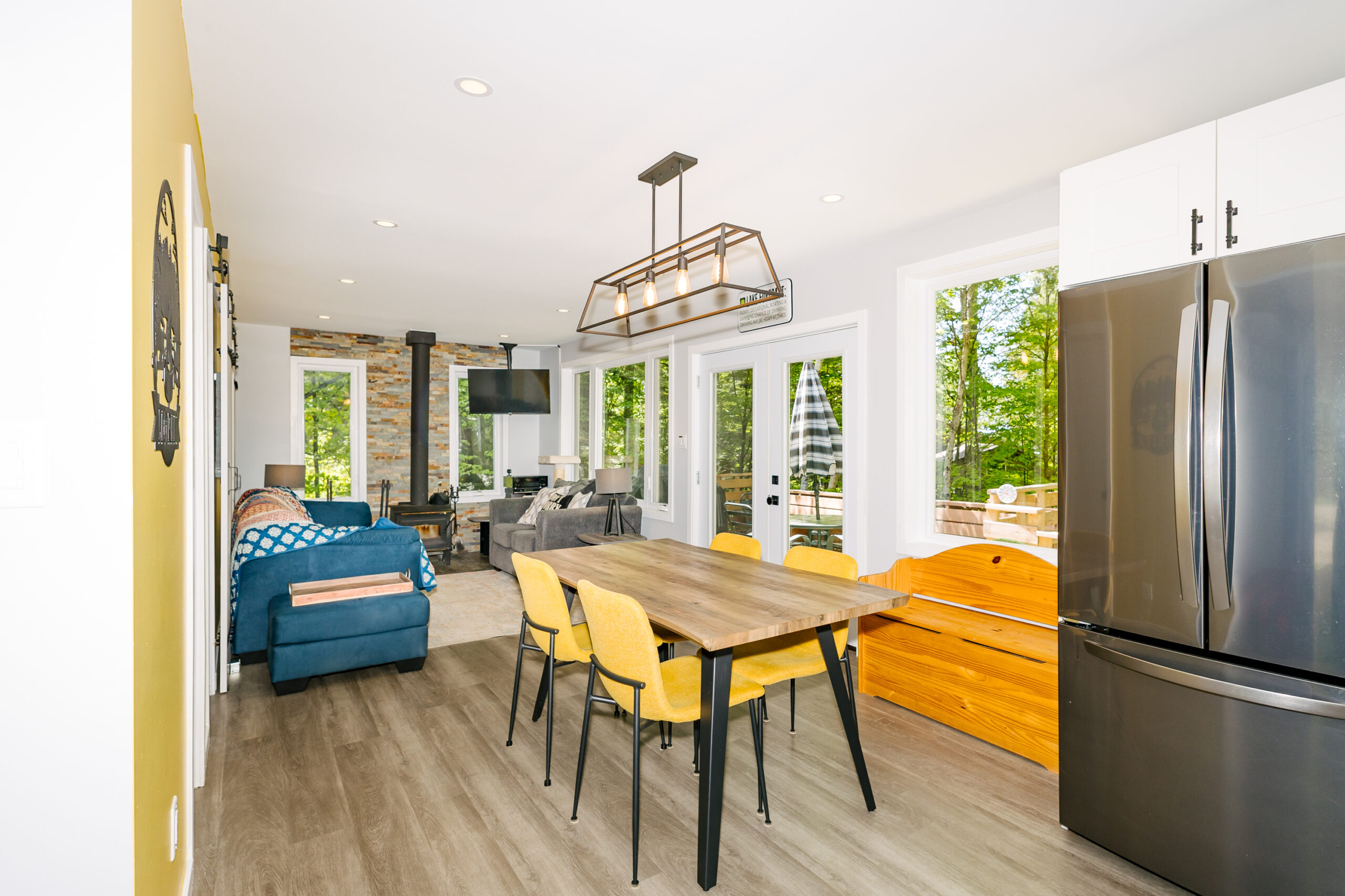Small wood dining table with yellow chairs faces glass doors to the upper-deck. To the left, a blue couch