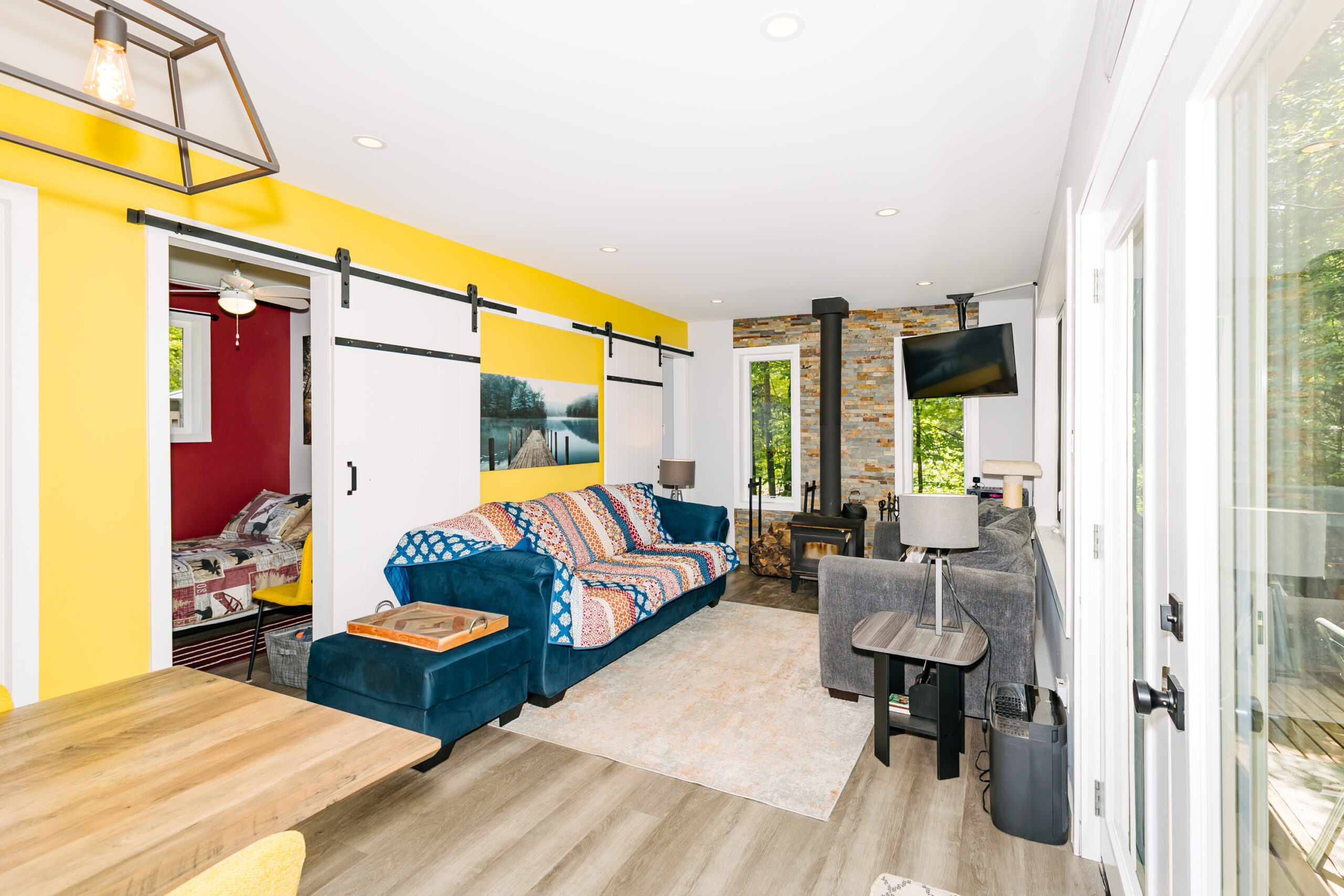 A blue couch with a patterned blanket on the back faces a grey couch. A small wood stove between the two