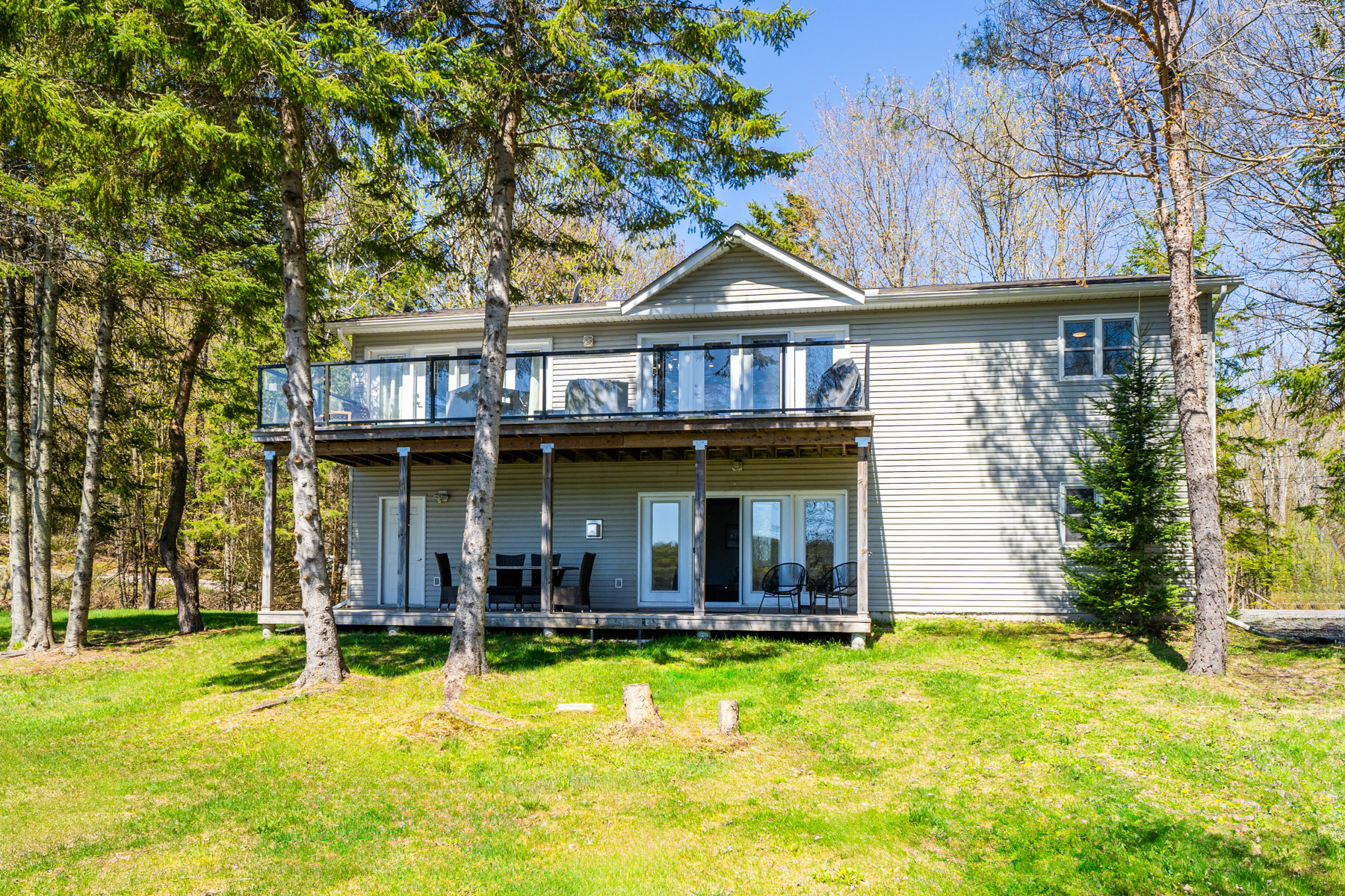 A two-level deck. On the lower level, a dining table and doors to the inside. The top has glass railings