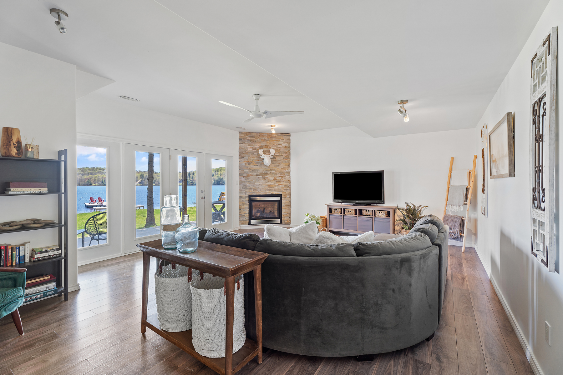 A velvety grey couch faces window-pane doors that face the lake and a fireplace