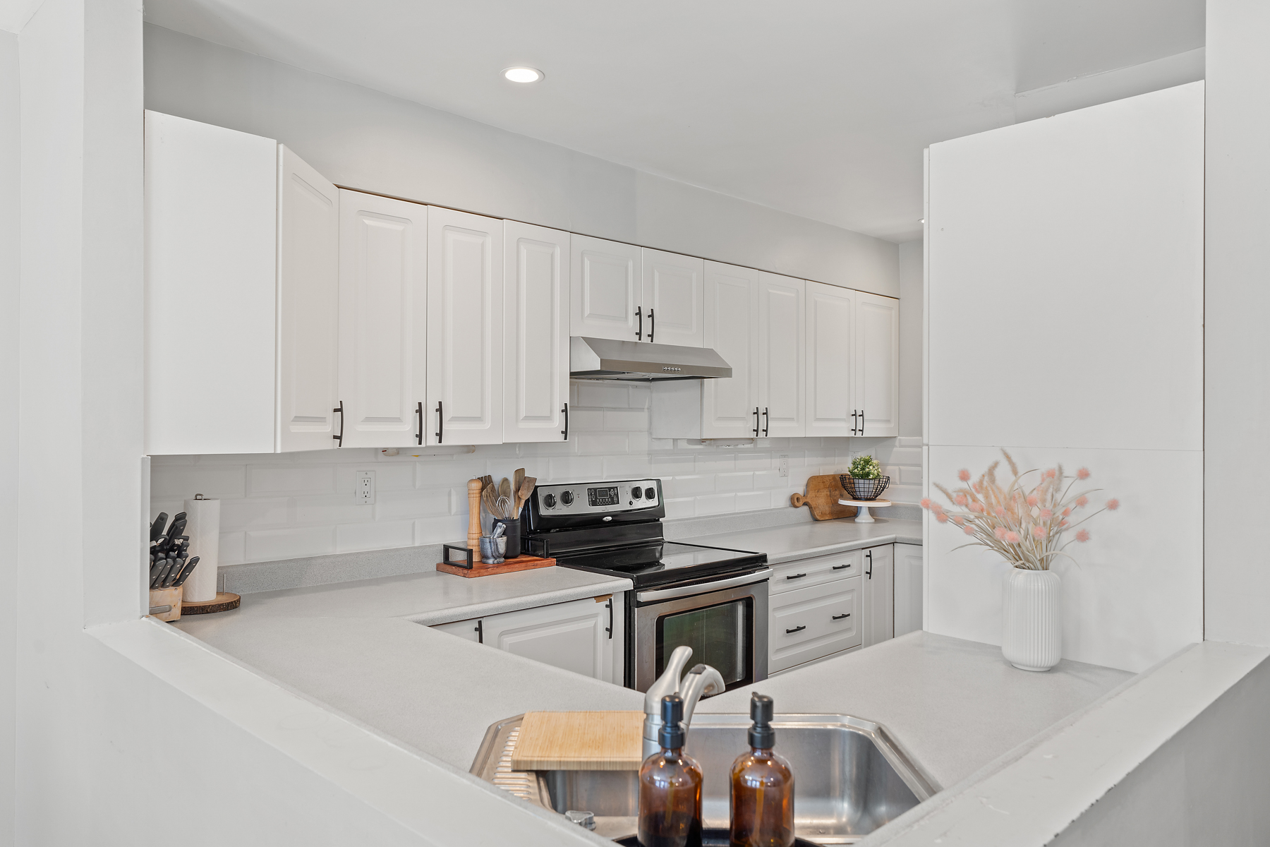 A stainless steel kitchen sink is in the corner of the kitchen countertops, across from the oven