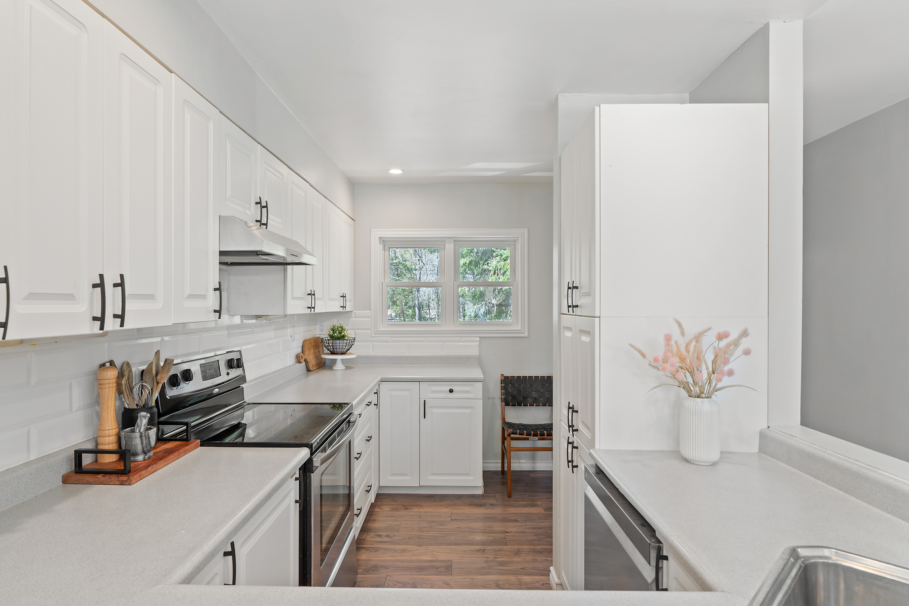 A narrow white kitchen with stainless steel appliances