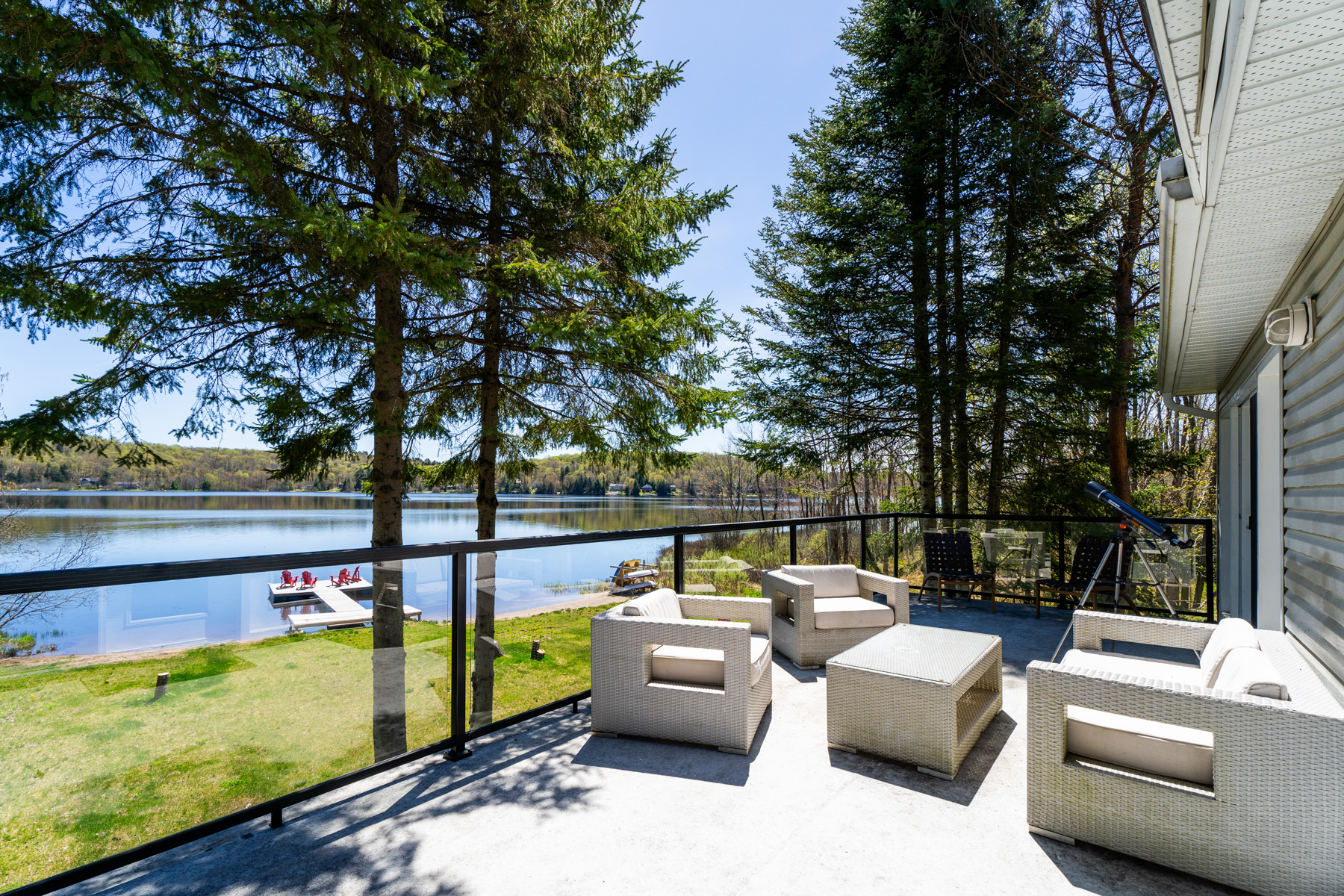 The upper deck, with glass railings, features cream coloured square deck furniture that overlooks the lake
