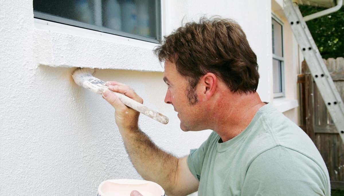 a caucasian man painting the exterior of a house