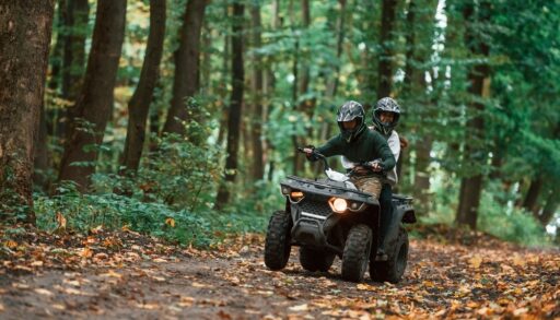 Two passengers riding an ATV on a trail in the woods
