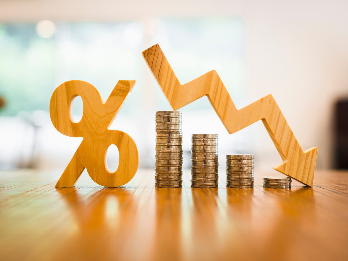 A wooden percentage mark is to the left of stacks of coins. An arrow pointing downwards hovers over the coins