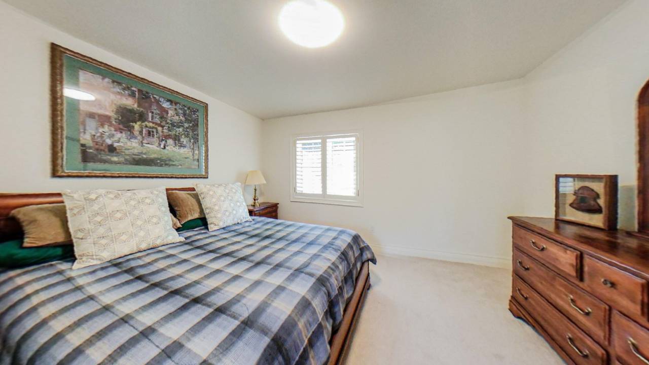 A blue checked bed faces a small window in a white room