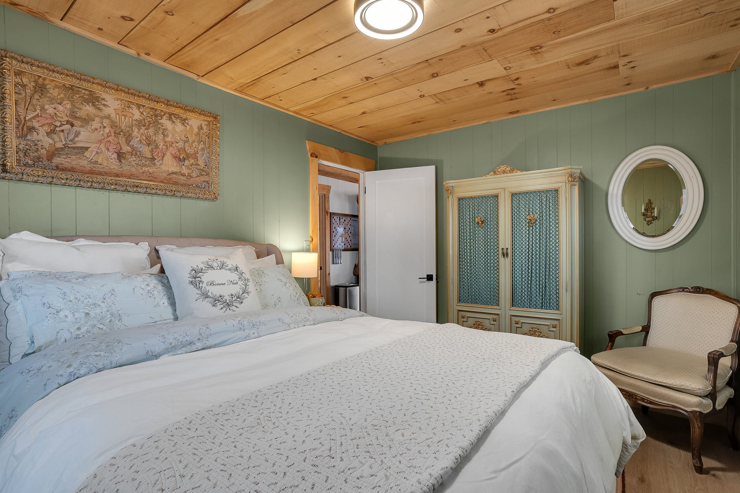 A large bed in a green room with wood panelled ceilings