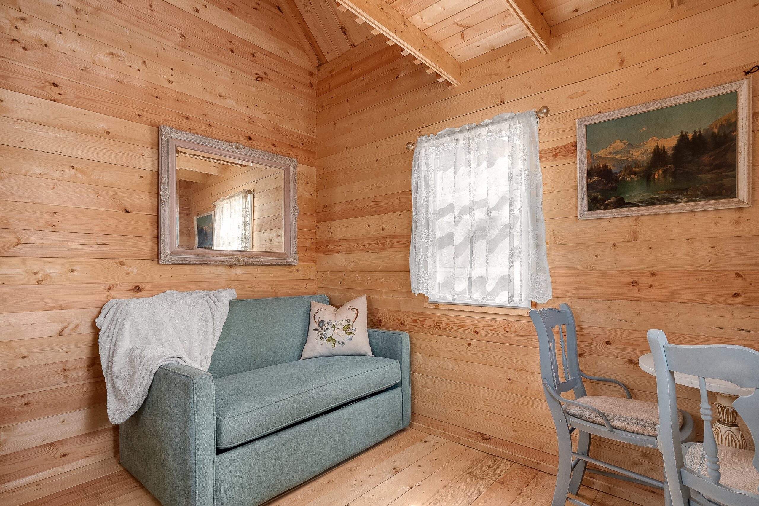A turquoise loveseat with a mirror above in a wood room