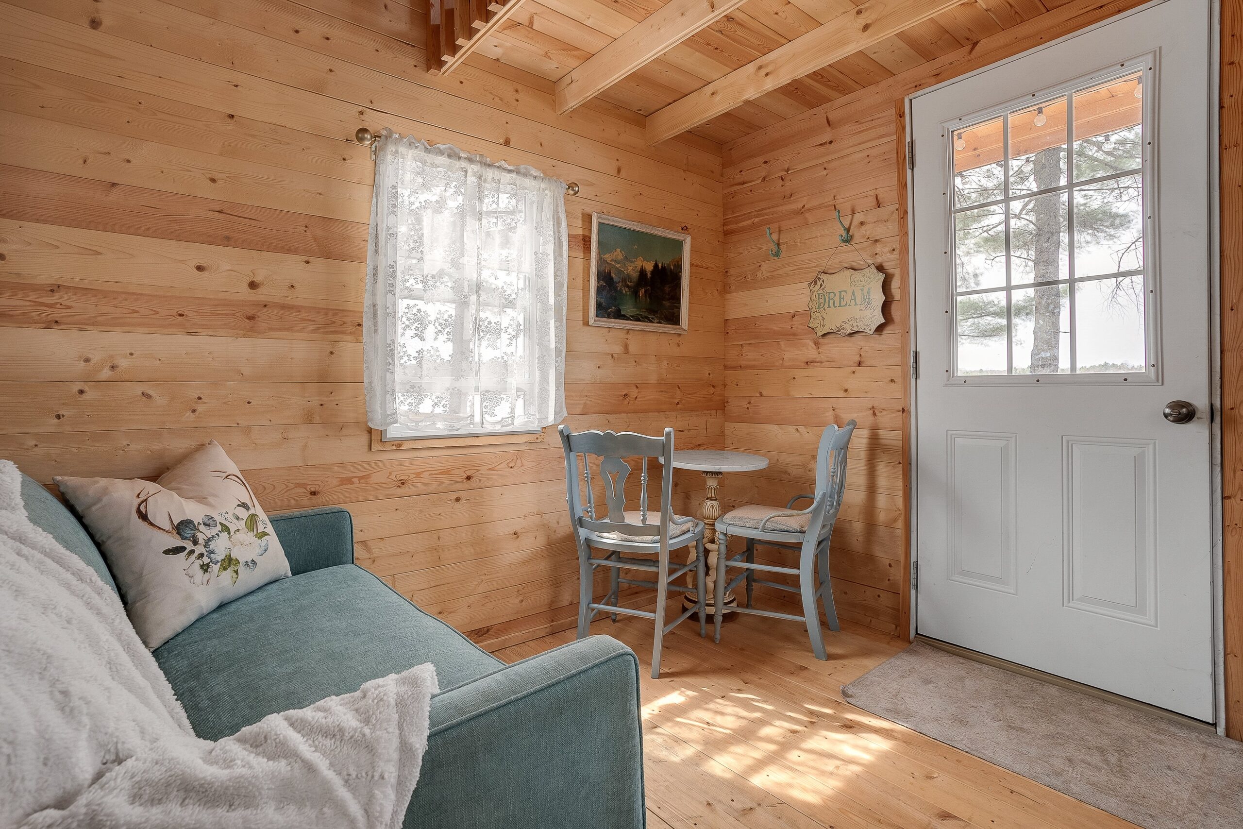 A wood interior with a teal loveseat facing a white door next to a small table