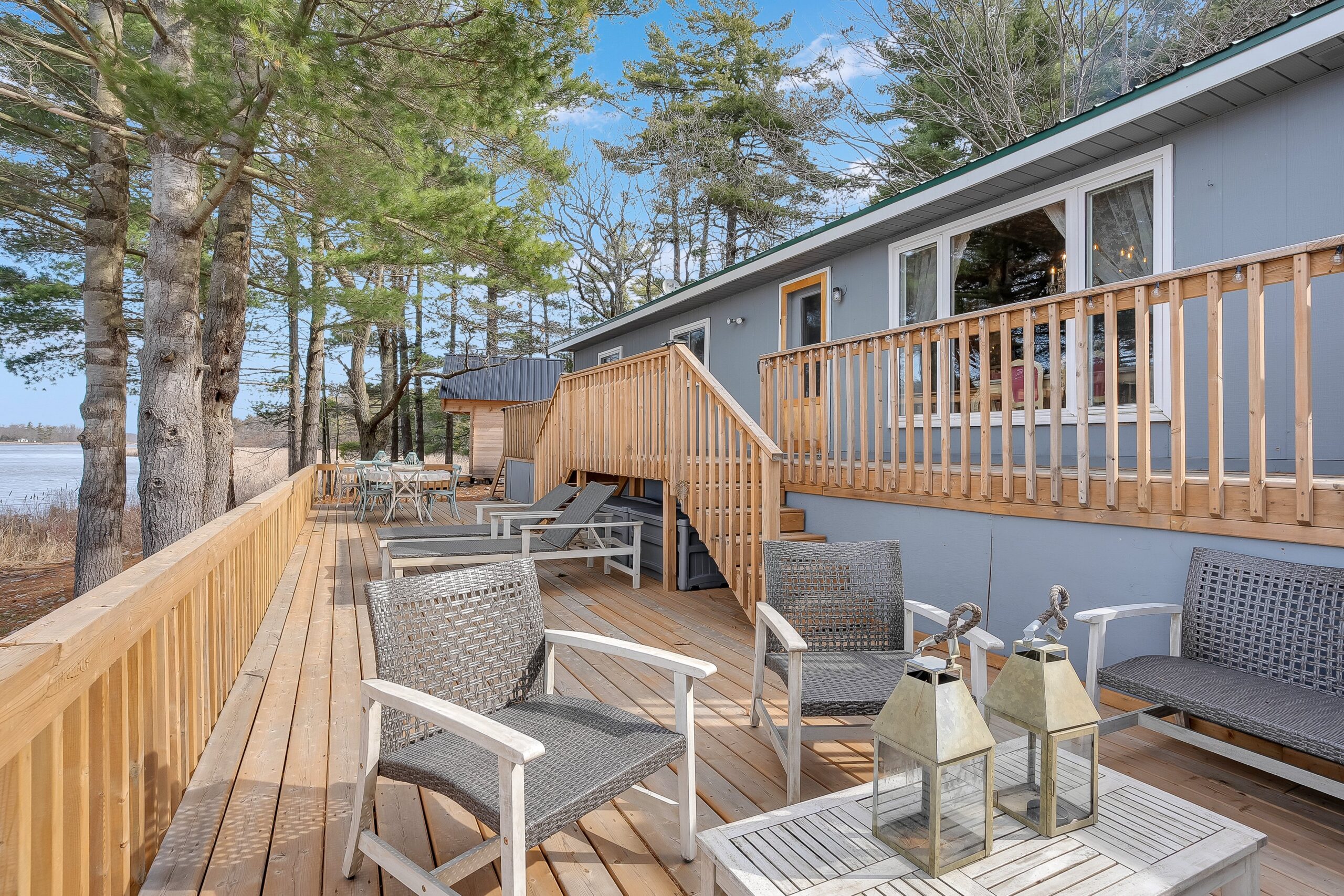 A two-level deck on the outside of a grey cottage leads to a sitting area