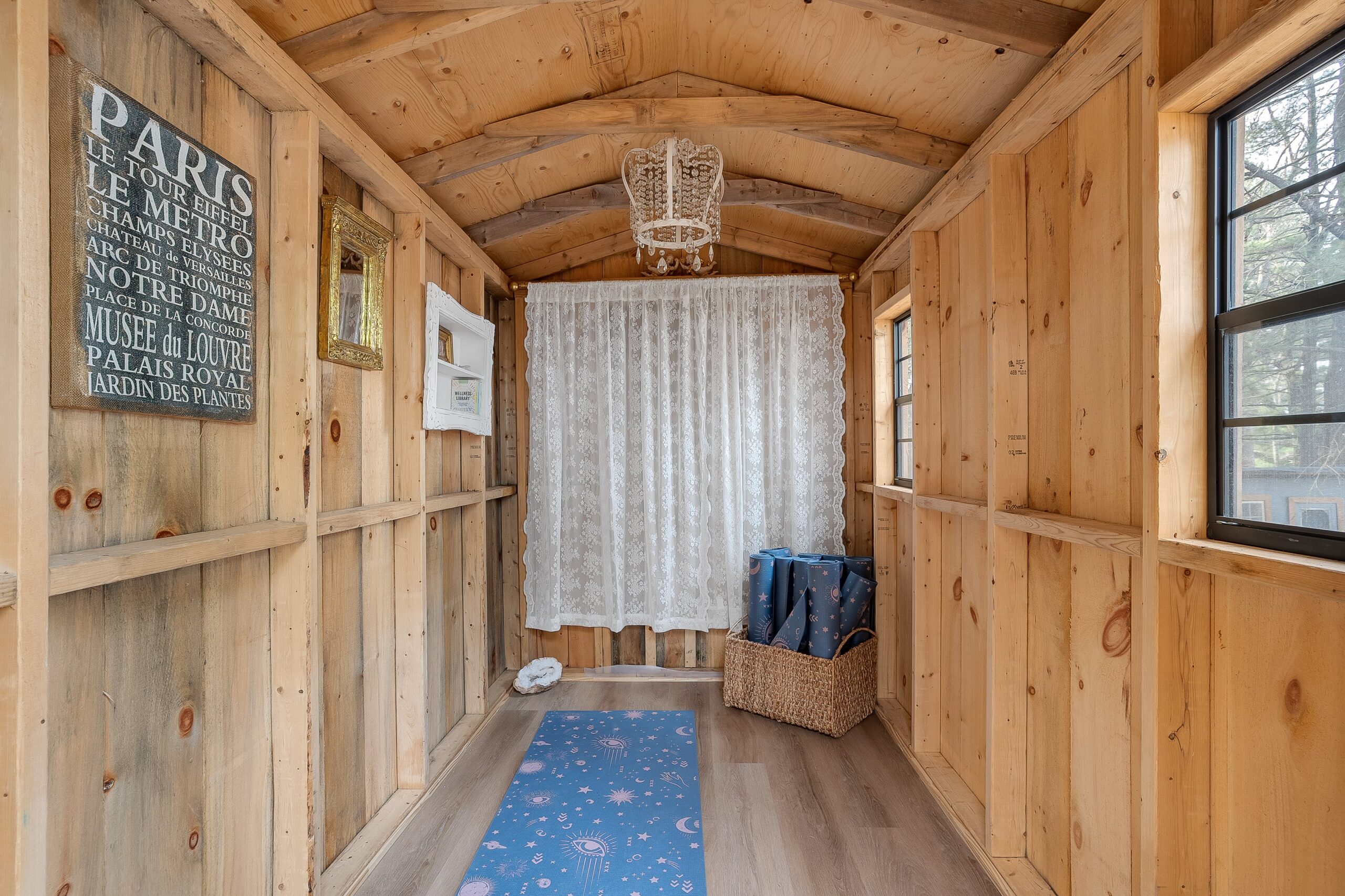 A blue yoga mat on the floor of a tiny wood cabin. A lace curtain shields a window behind