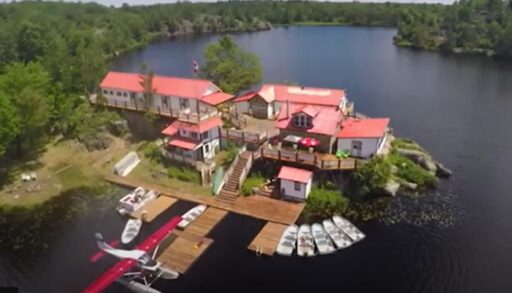 A sprawling white lodge with a red roof is surrounded by a lake.