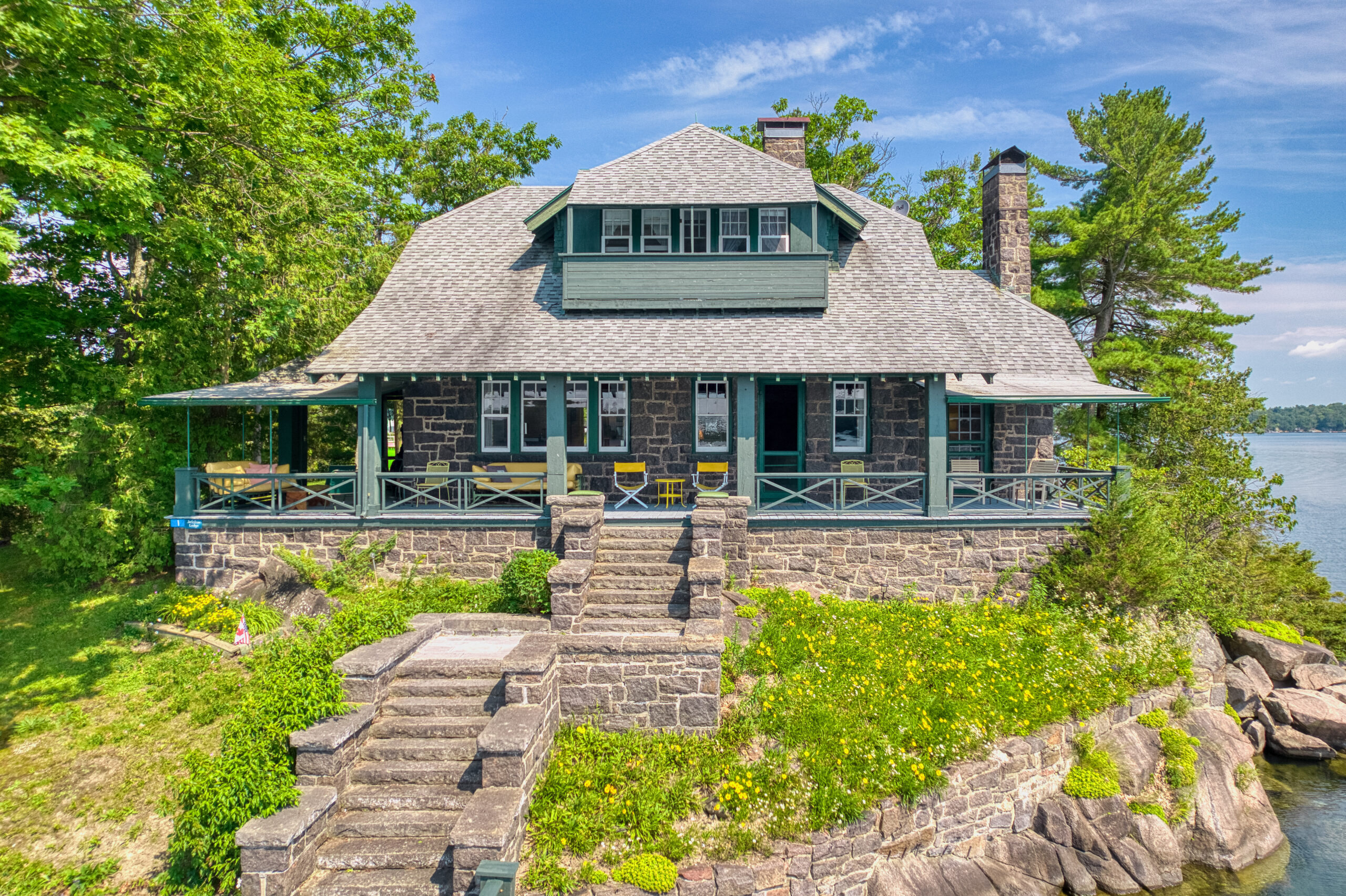 Large stone steps lead up to a stone two-level cottage with green trim