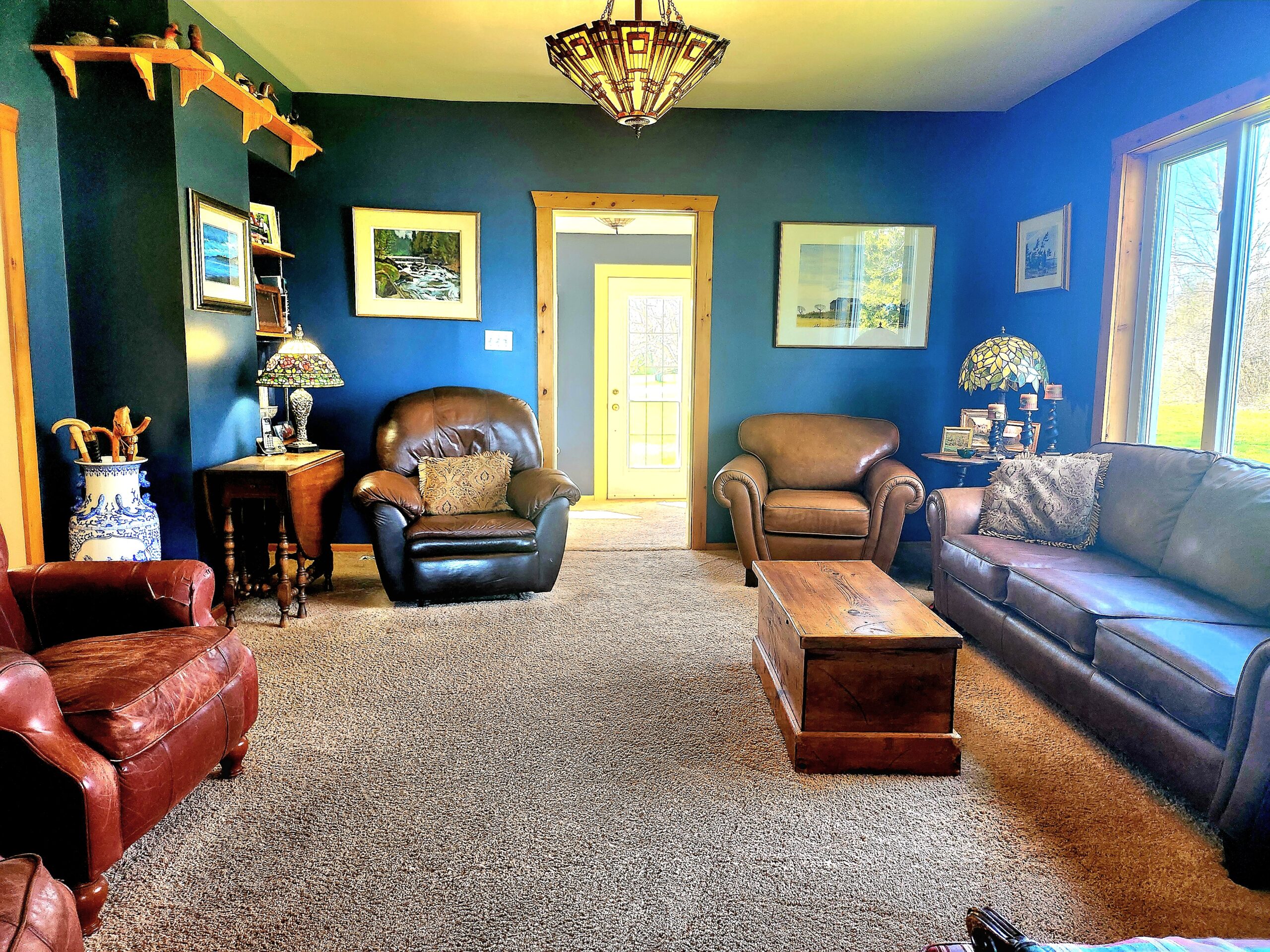 A blue painted room with a leather couch in the right side facing a wood coffee table. Across, a red leather couch faces it