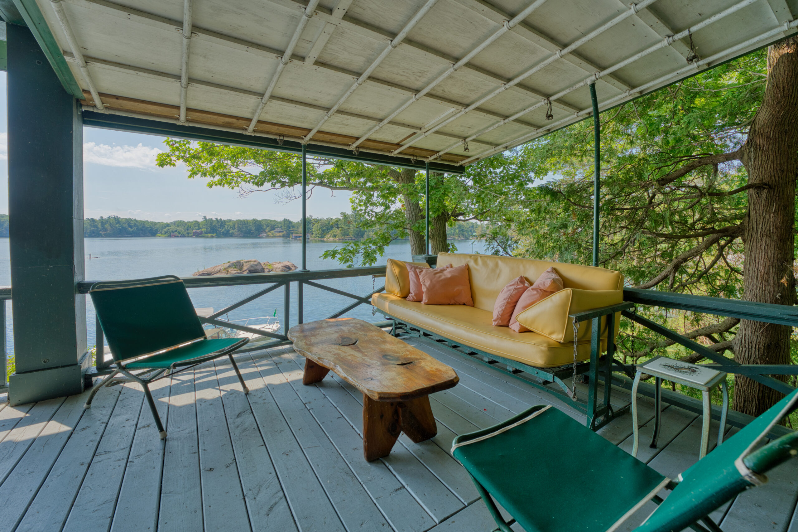 A porch swing with yellow cushions face a wood coffee table on the porch outside the cottage