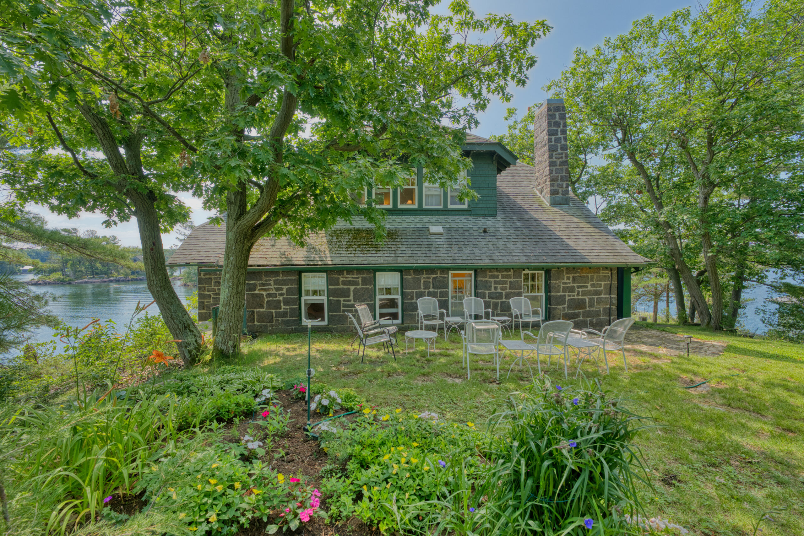 A stone cottage with a grassy clearing. In the grass, white chairs sit in the circle