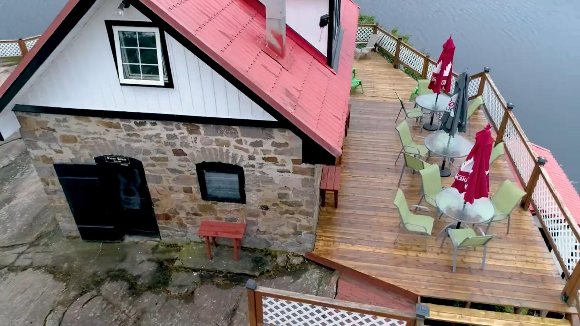A stone house with a red roof next to a wood deck with green chairs