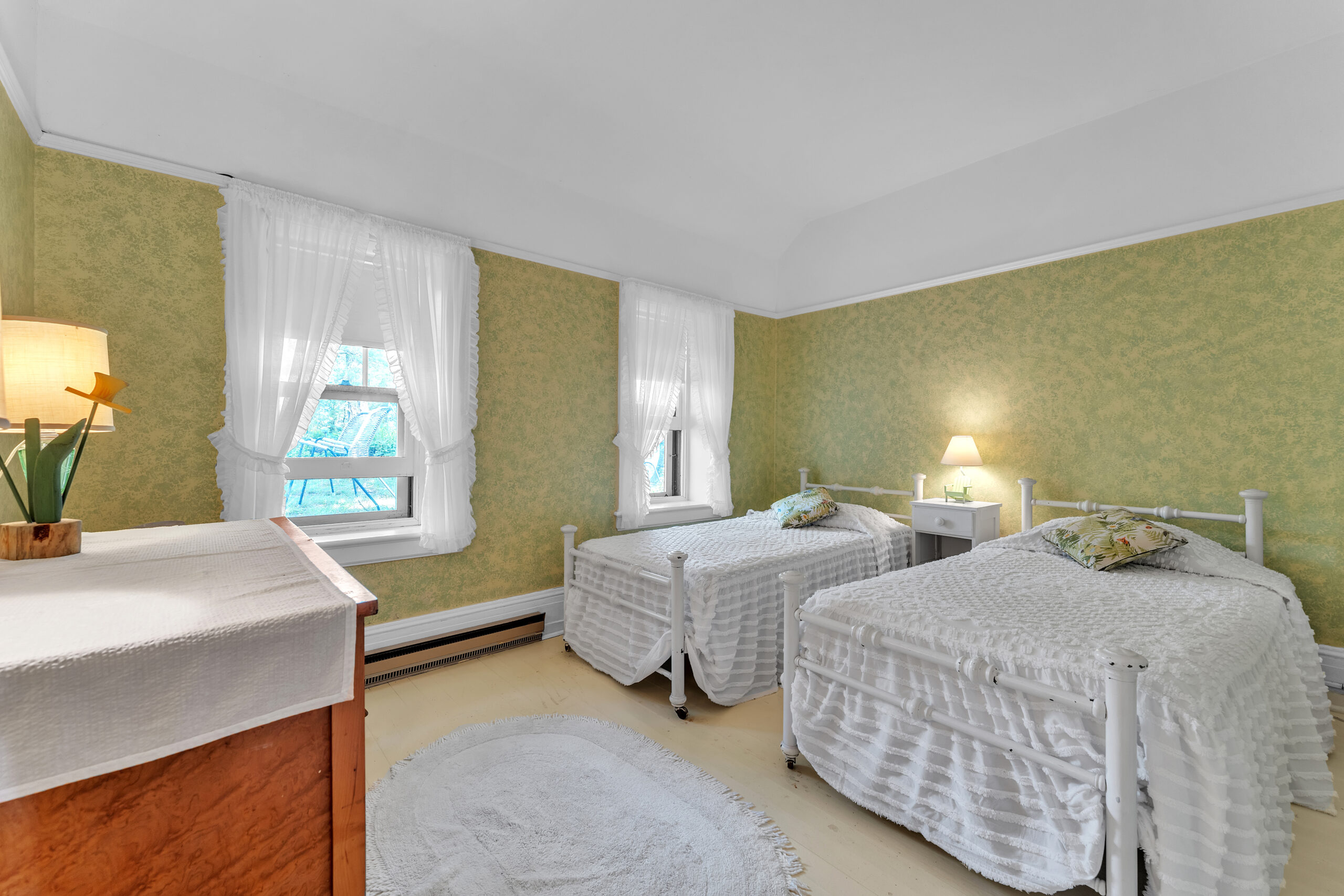 Two white beds face a dresser in a green bedroom