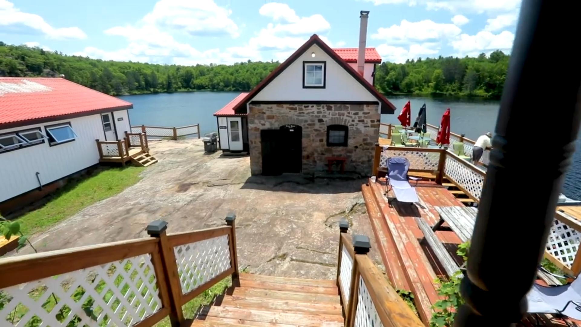 Wood steps lead to a stone house with a red roof on a stone patio