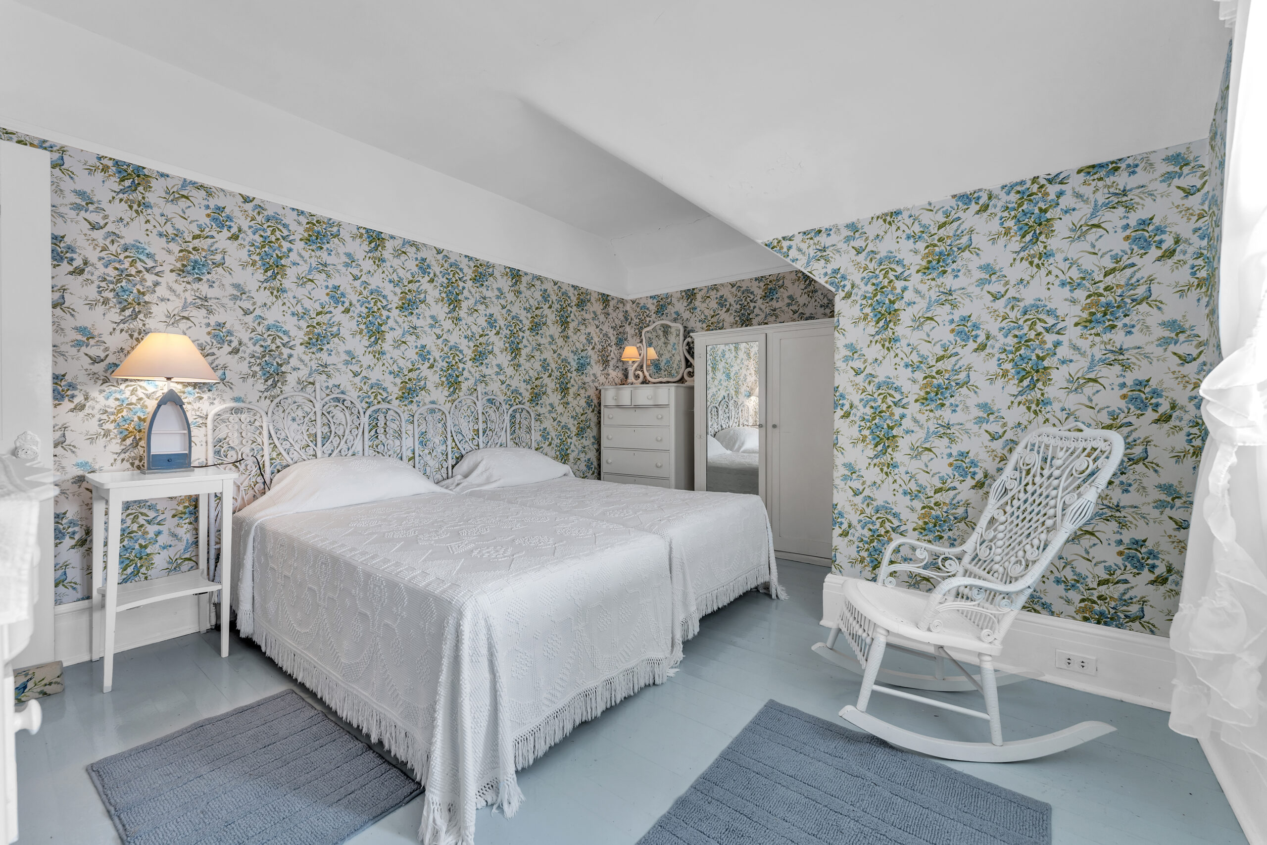 Two white beds pressed against each other in a wallpapered room