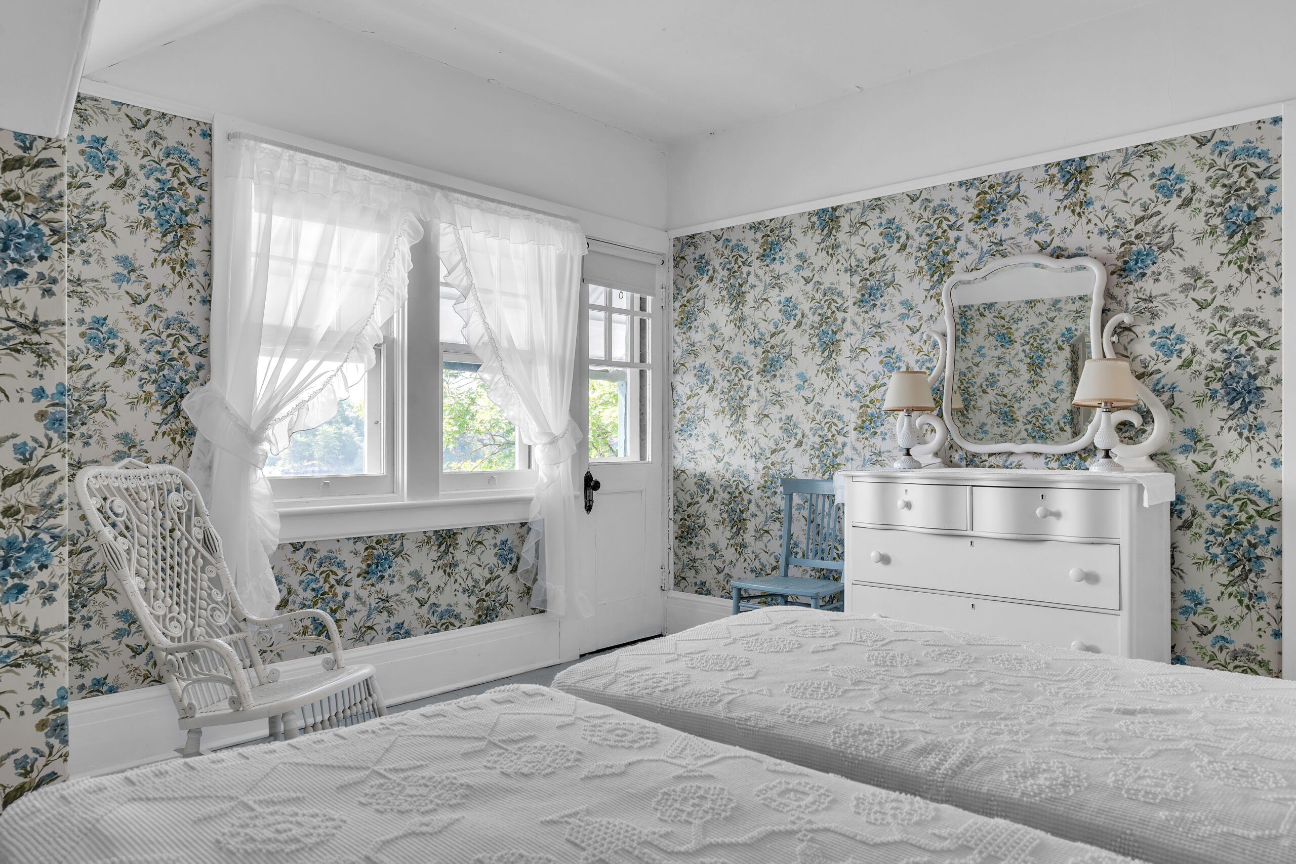 Two white beds face a bright window with sheer curtains