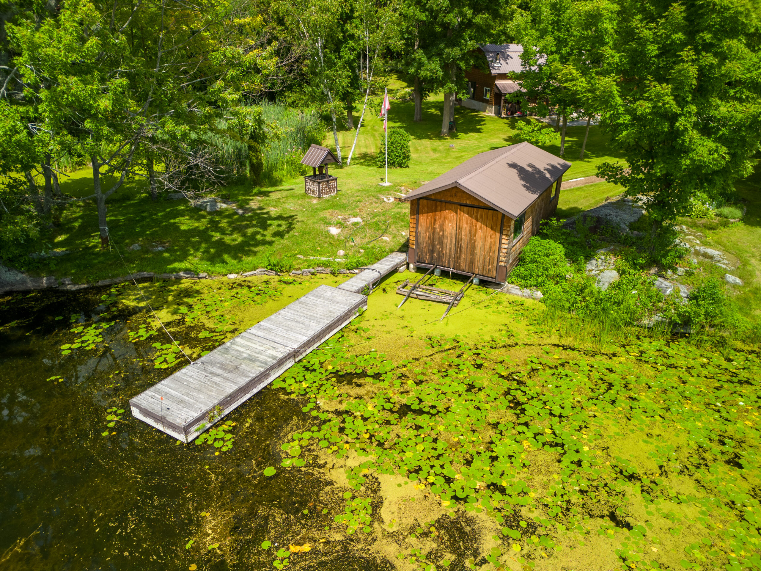 A boathouse at the edge of a grassy lawn with a long dock that goes into a green lake