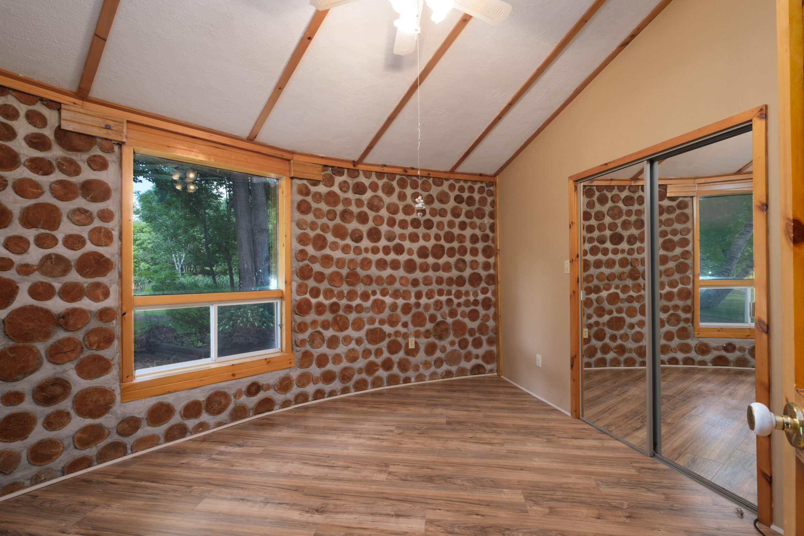 A rounded room with wood floors and a stone wall with a large window