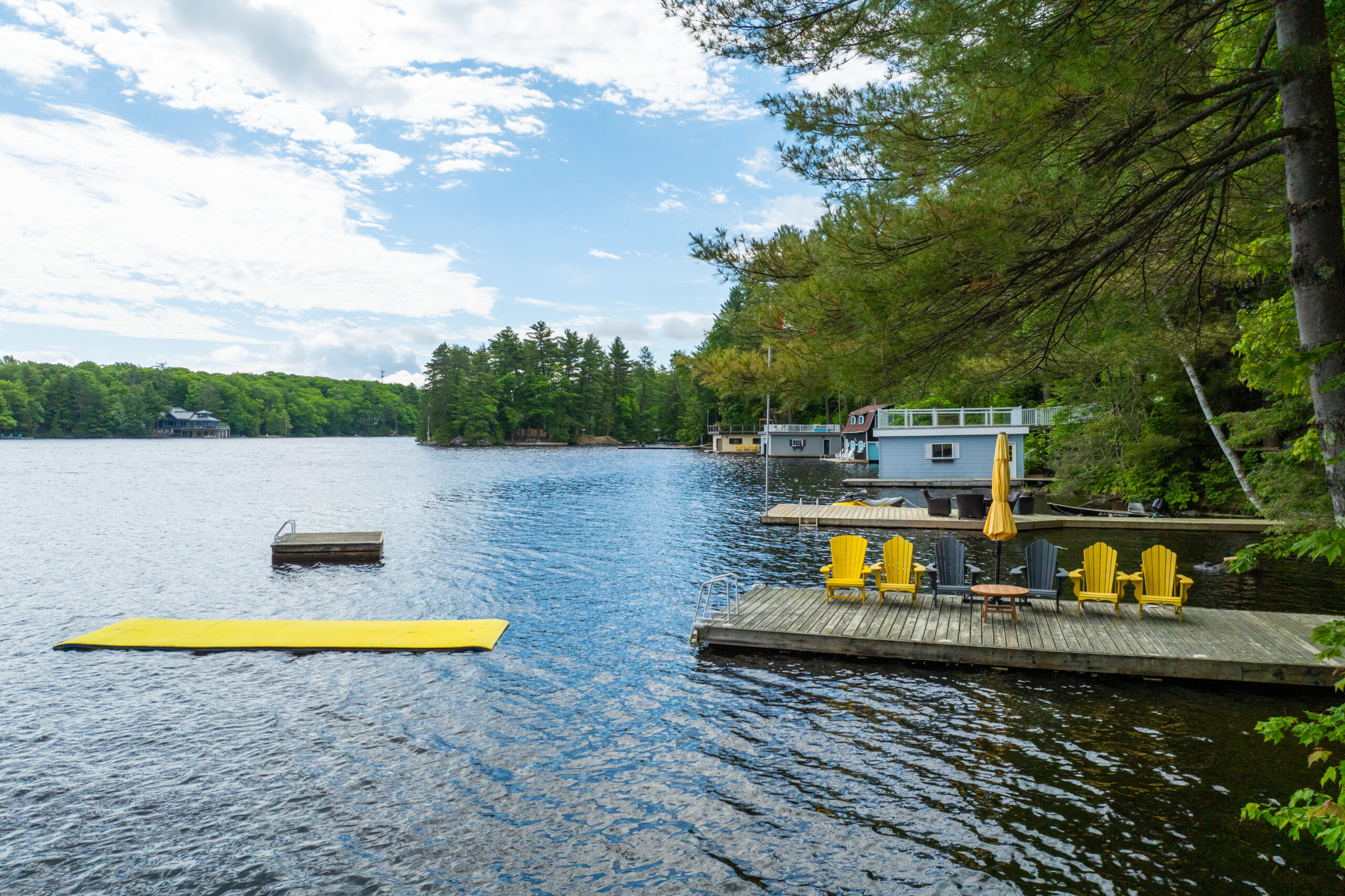 A dock with yellow Muskoka chairs. To the left, a yellow floating mat in the lake