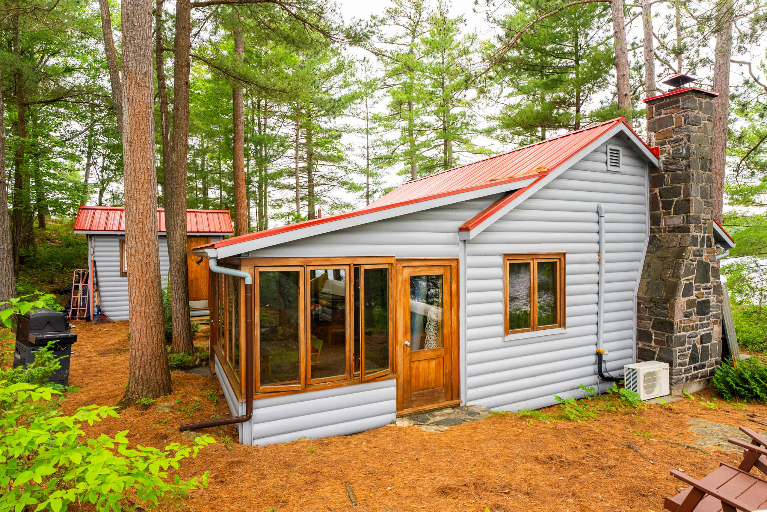 A grey cottage with a red roof and a large, wood-trimmed windows