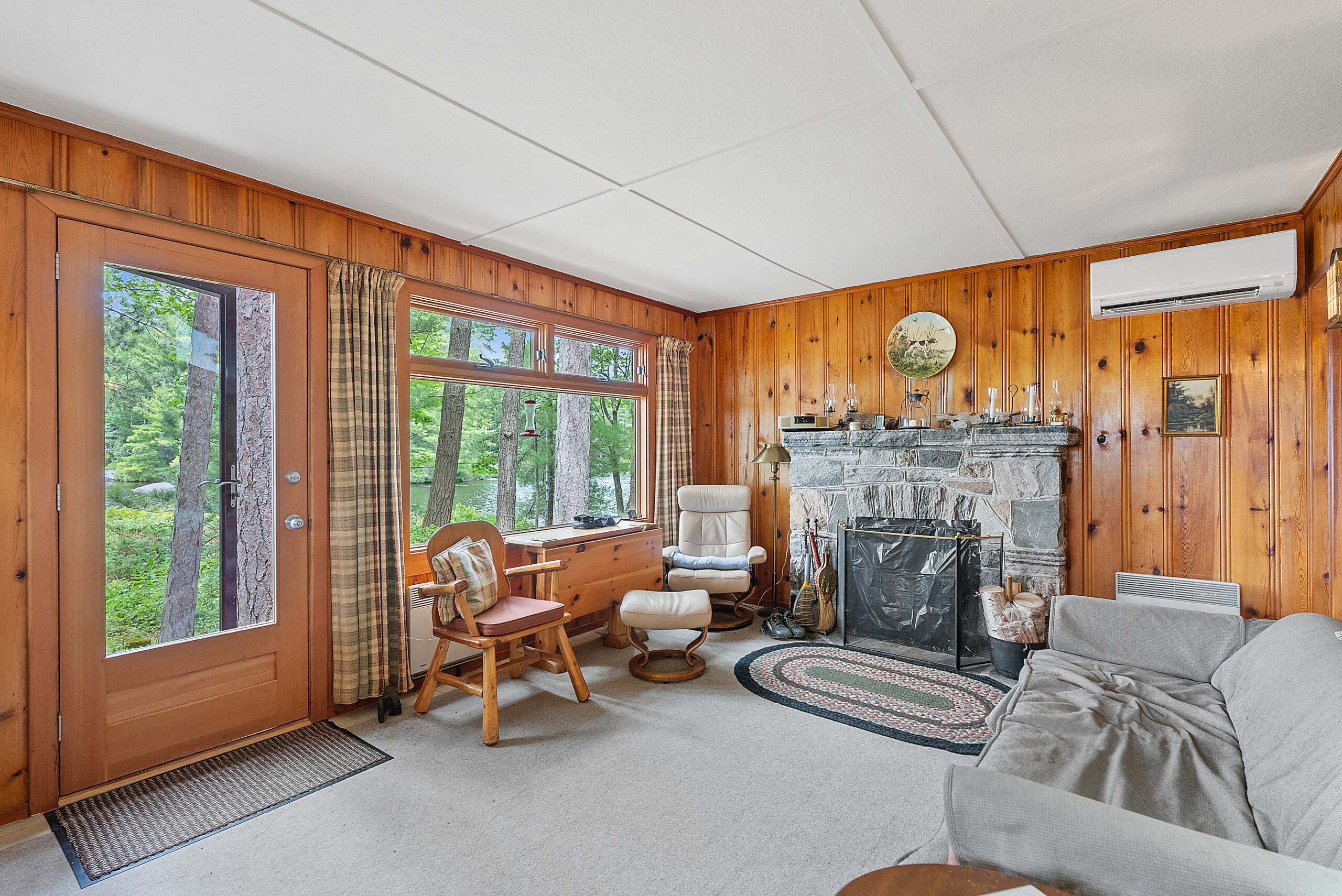 A brown wood chair is against bright windows, perpendicular to a stone fireplace