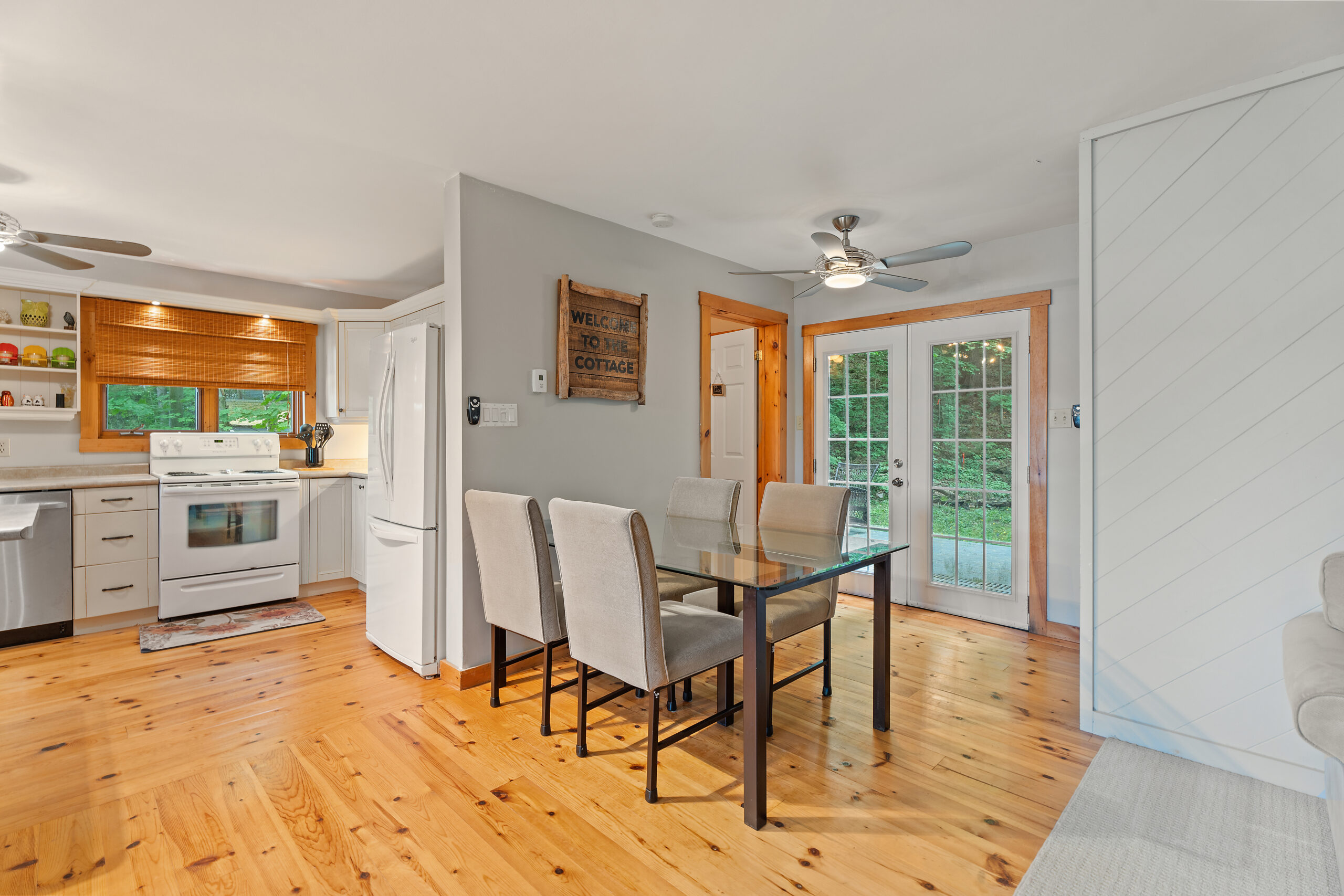 A dining table with white chairs meet a white wall. The table faces white French doors