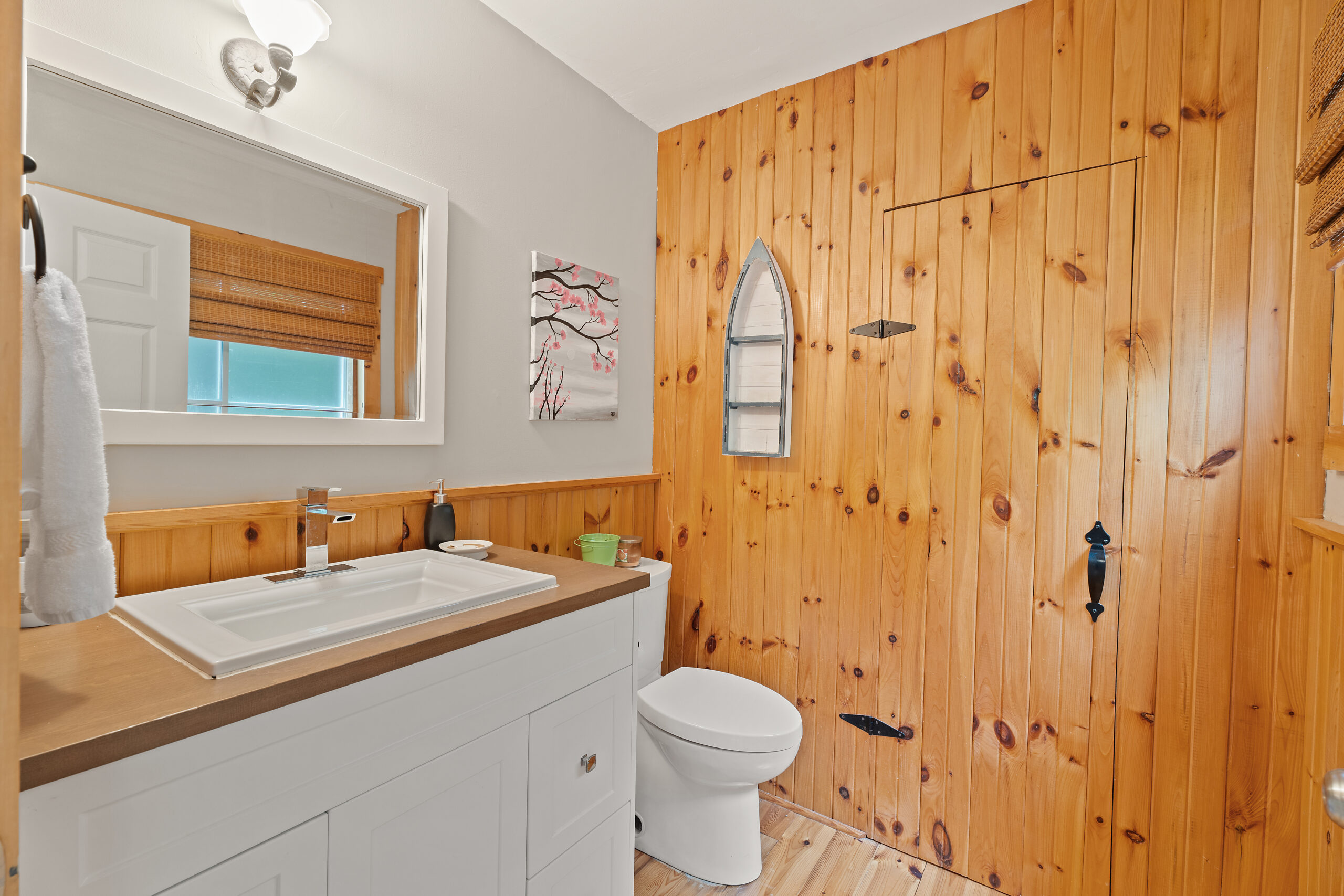 A wood-panelled bathroom with a white toilet, white cabinets, and brown countertop