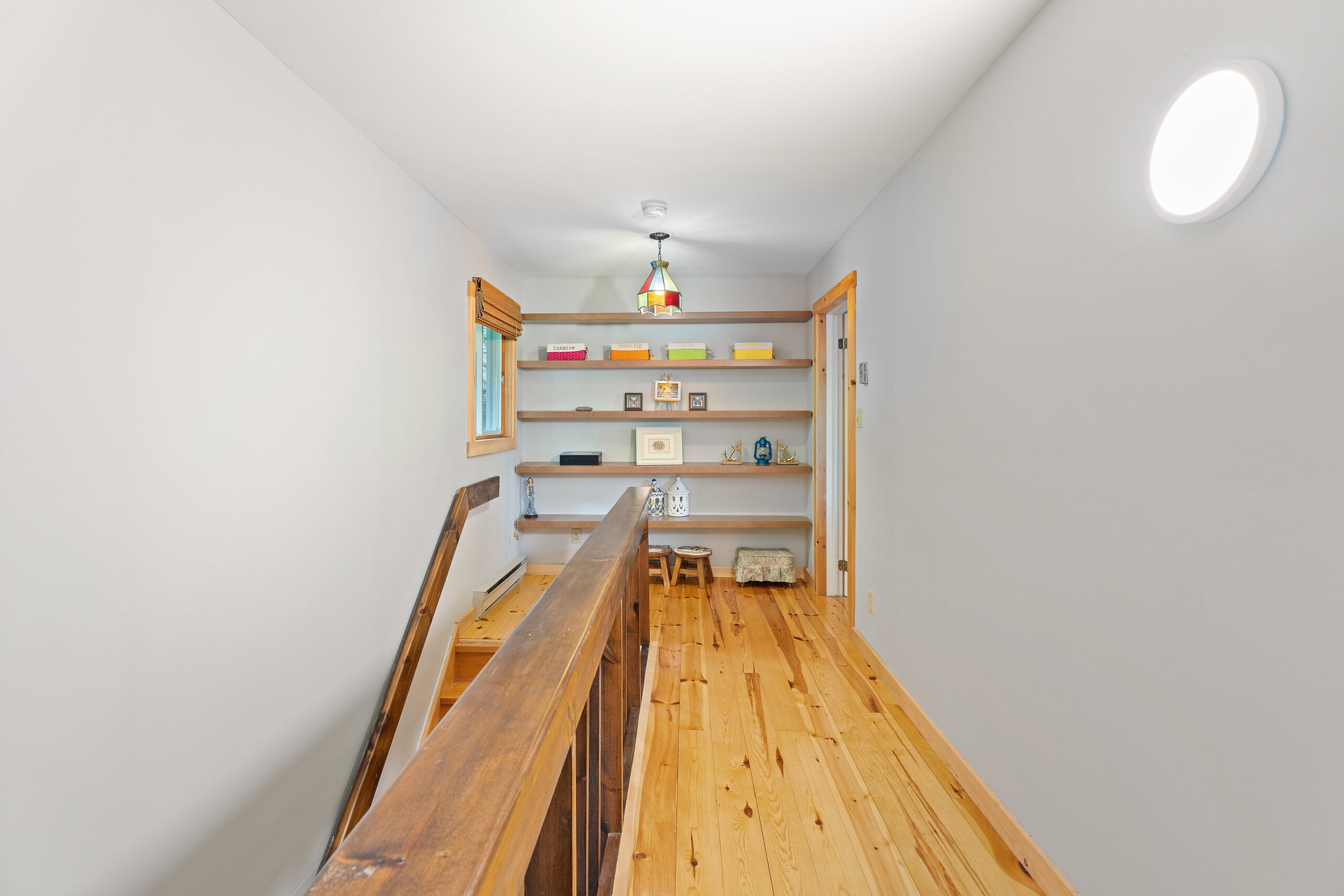 Second floor landing has light brown hardwood floors and wood floating shelves