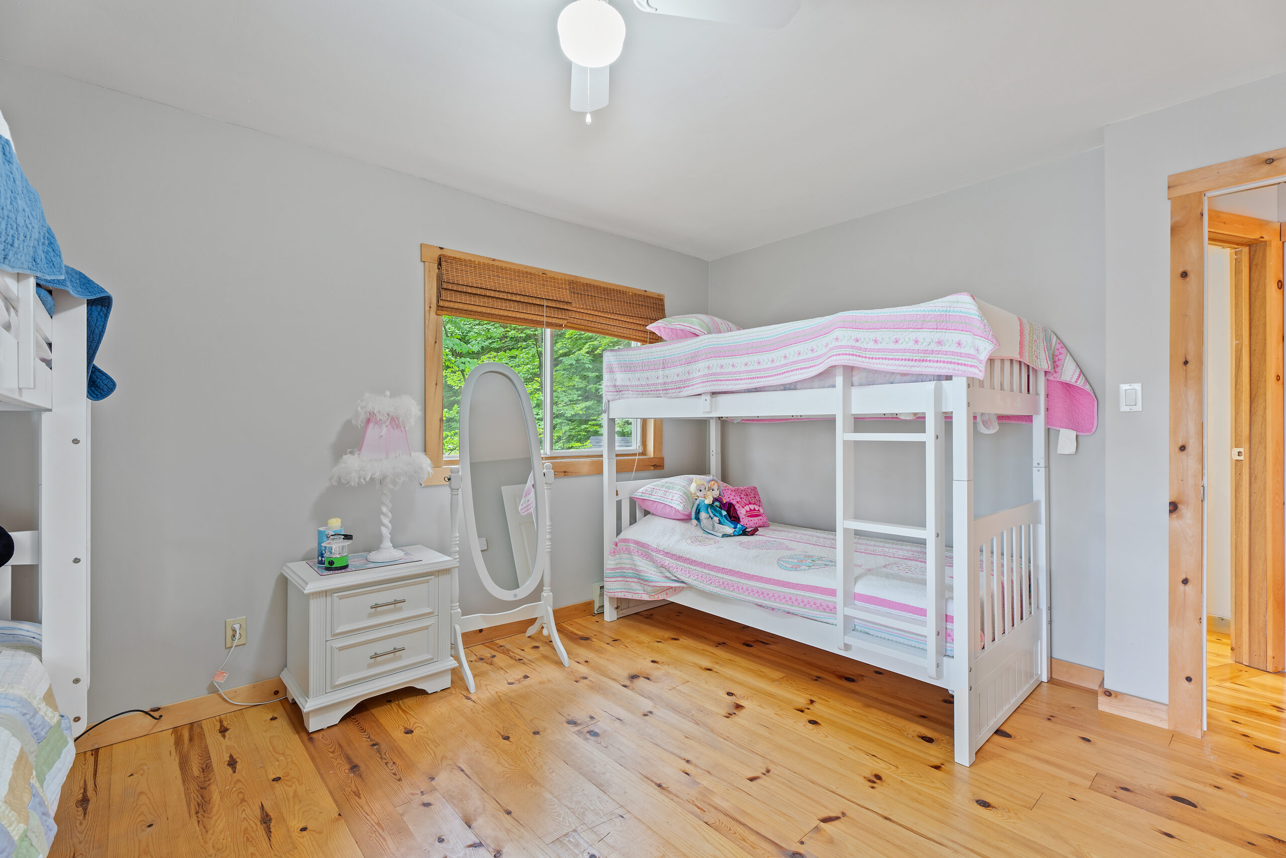 A white bunkbed with pink covers in a white room with wood floors