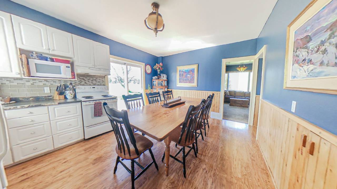 A blue painted kitchen with white cabinets. In the centre of the room, a wood dining table with chairs