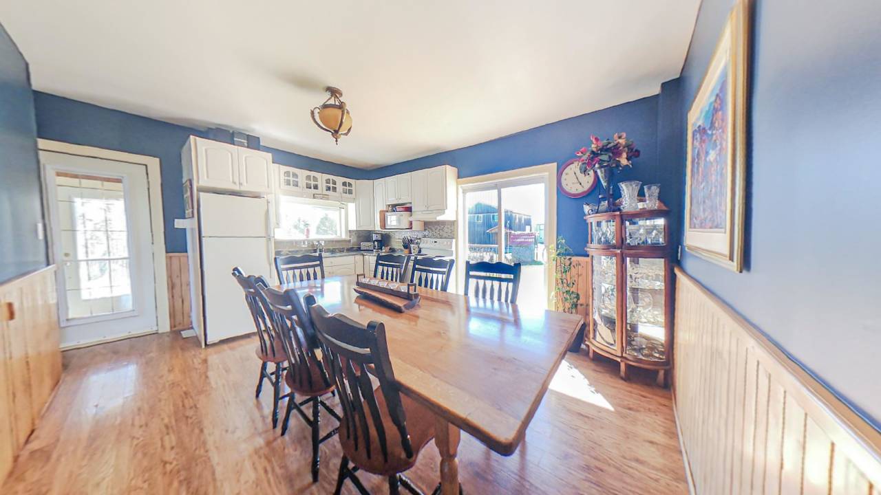 A blue painted kitchen with white cabinets. In the centre of the room, a wood dining table with chairs