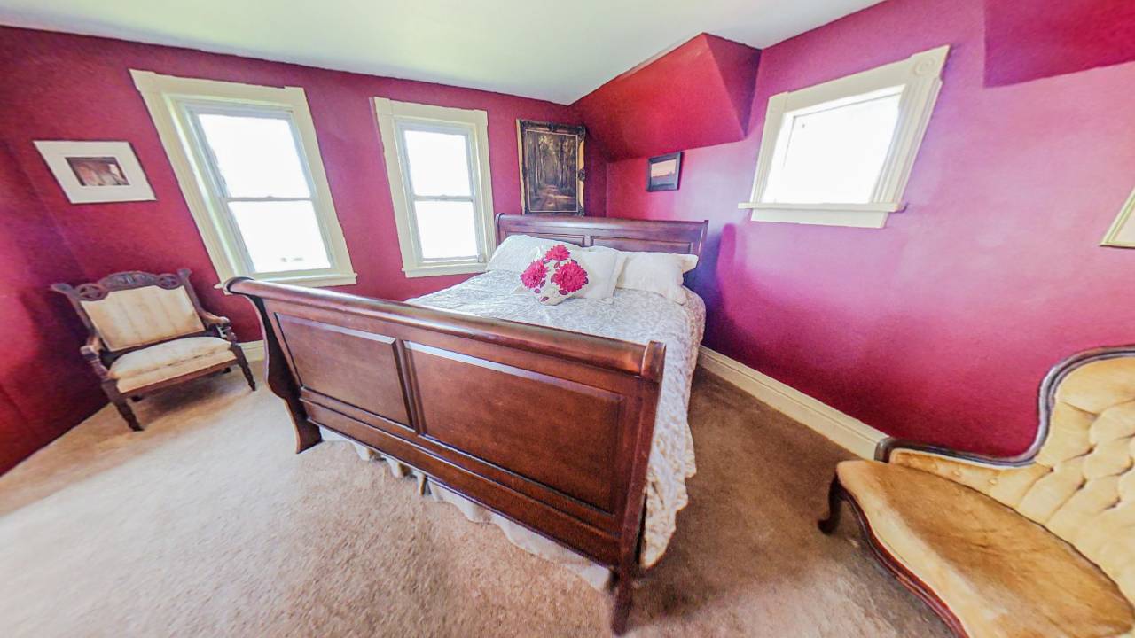 A large wood bed with a white bedspread in the corner of a red room