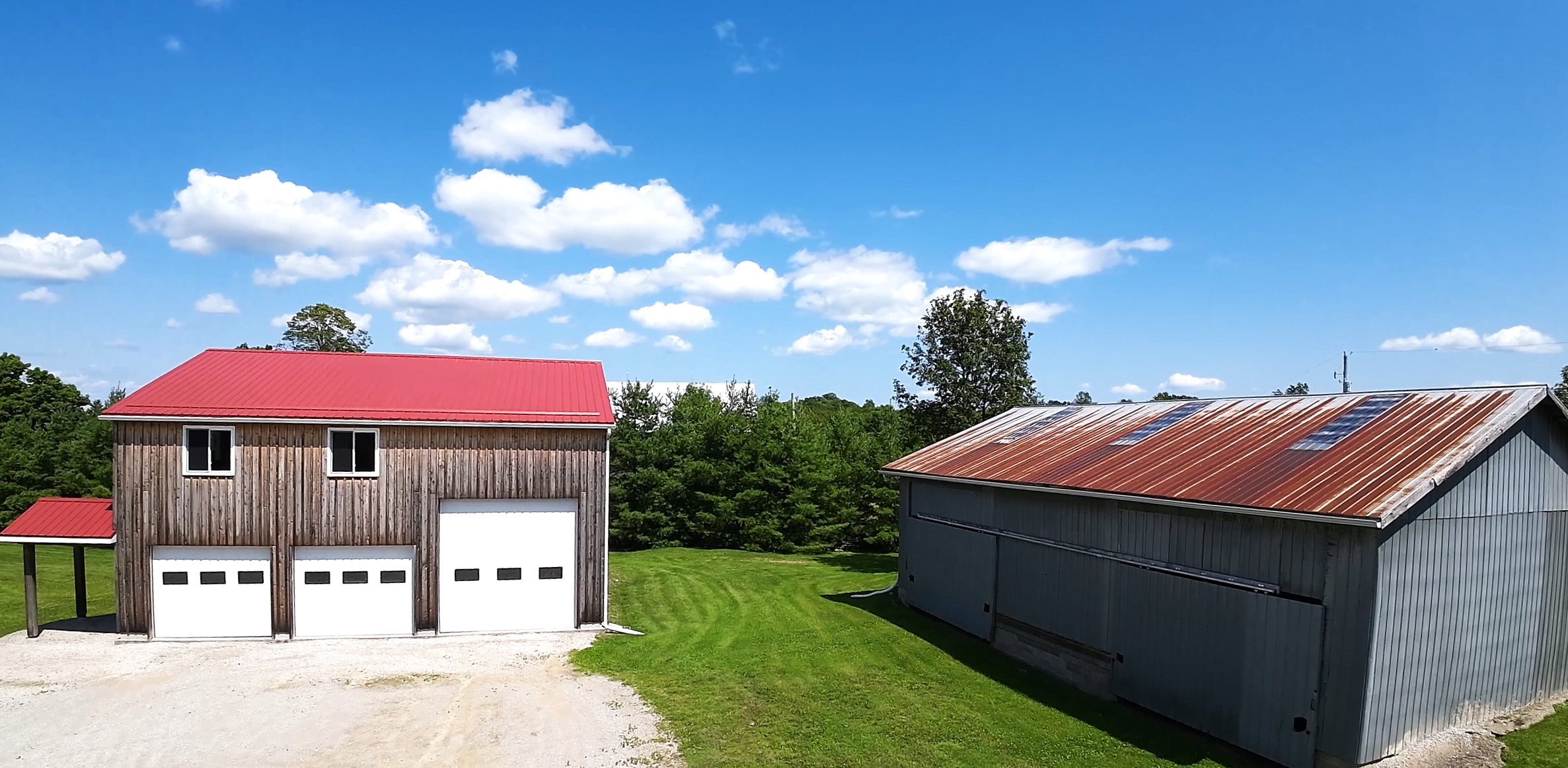 A brown garage with a red roof next to a grassy lawn and barn