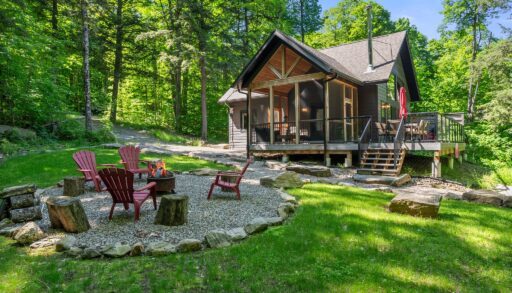 A wood cottage with a gravel fire pit area with red muskoka chairs