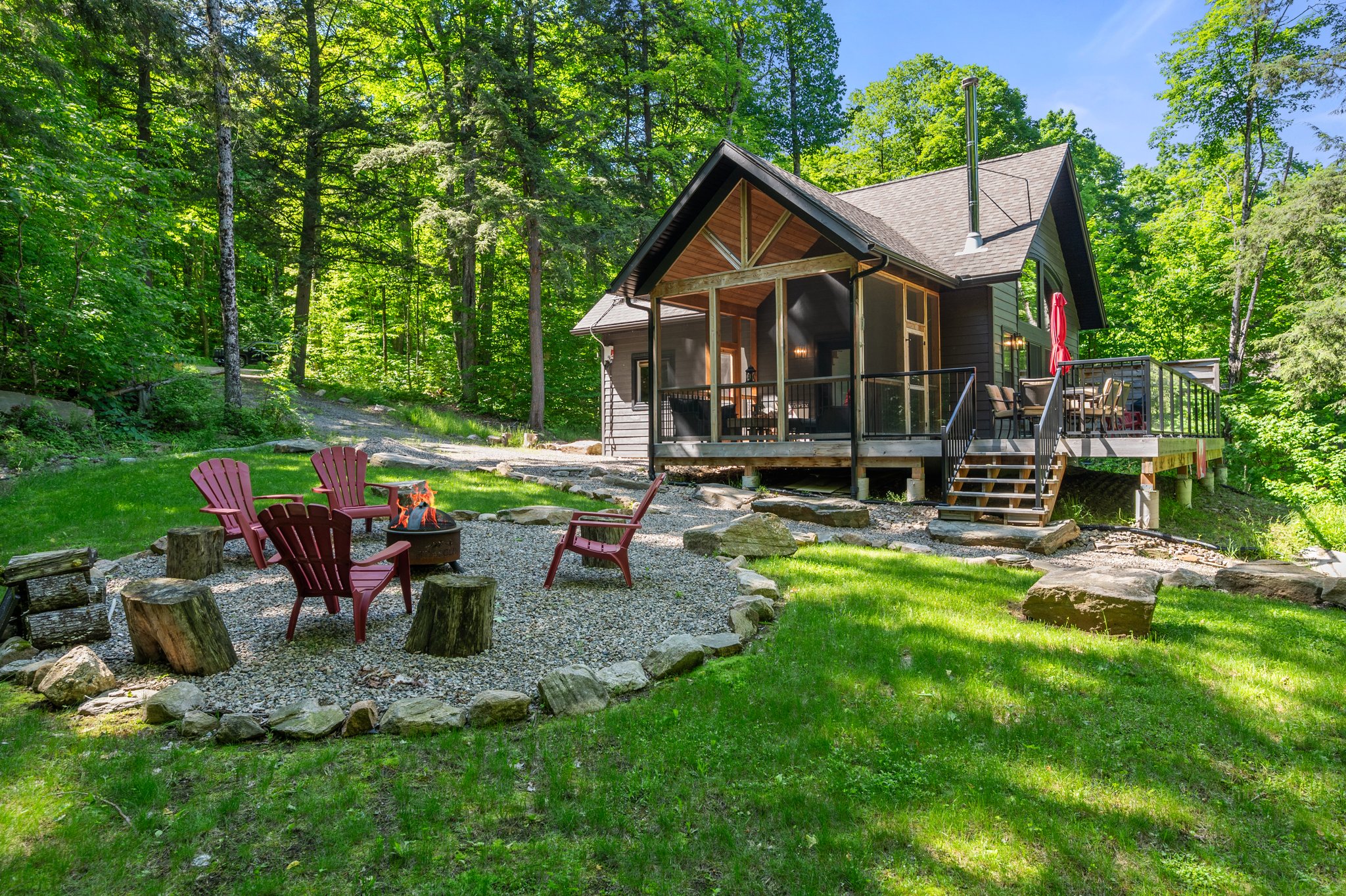 A wood cottage with a gravel fire pit area with red muskoka chairs