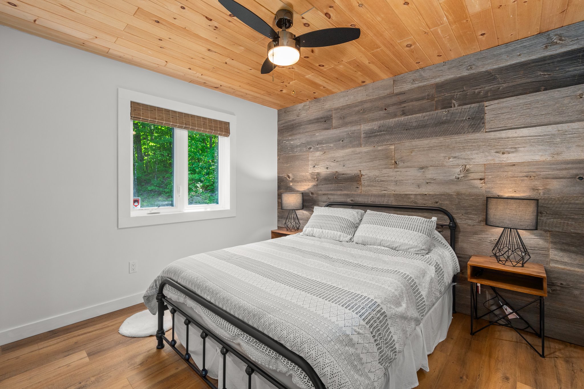A bed with a striped bedspread with a faux wood wall behind