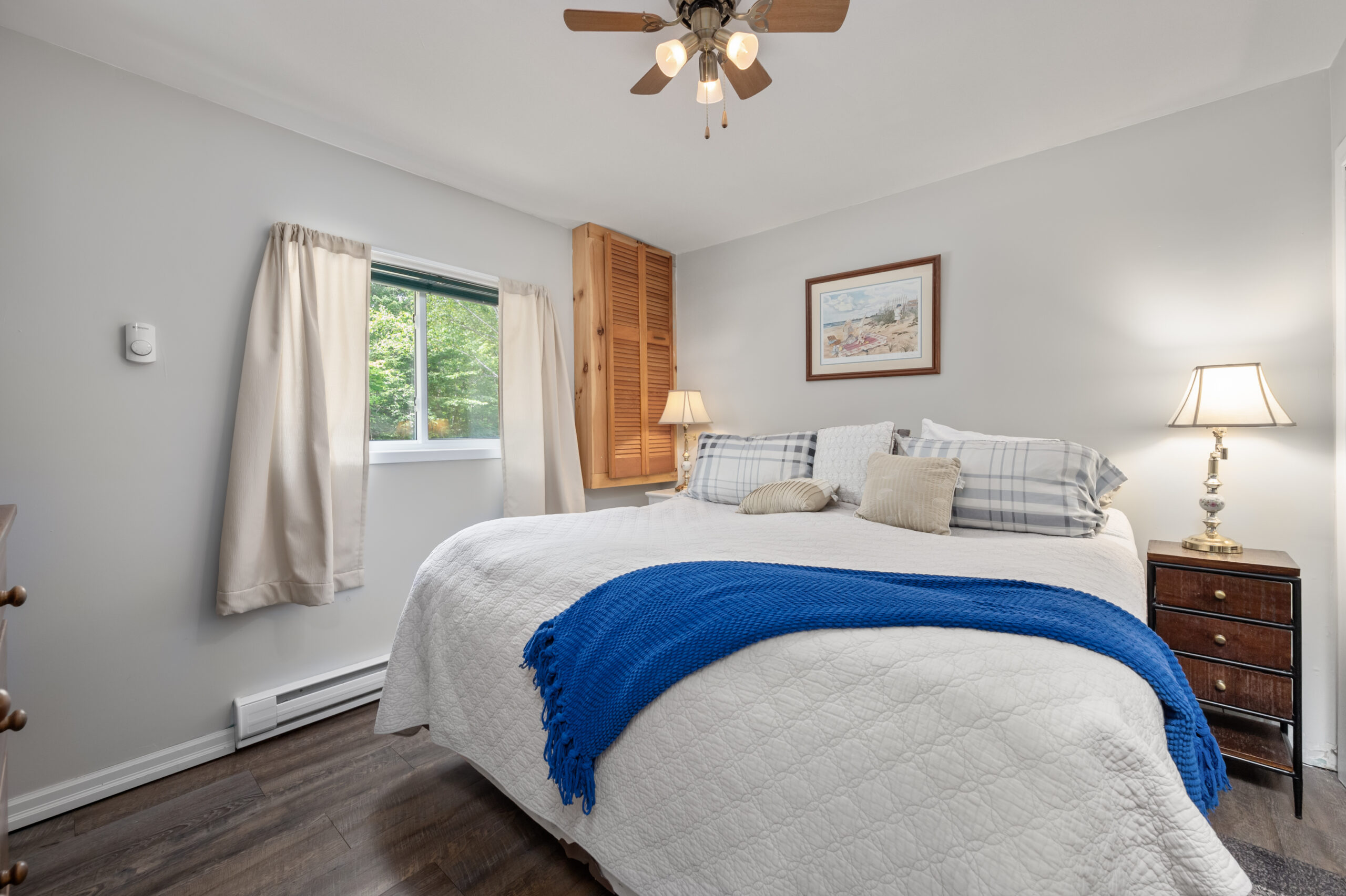 A large white bed with a blue blanket drapped over the end in a bedroom