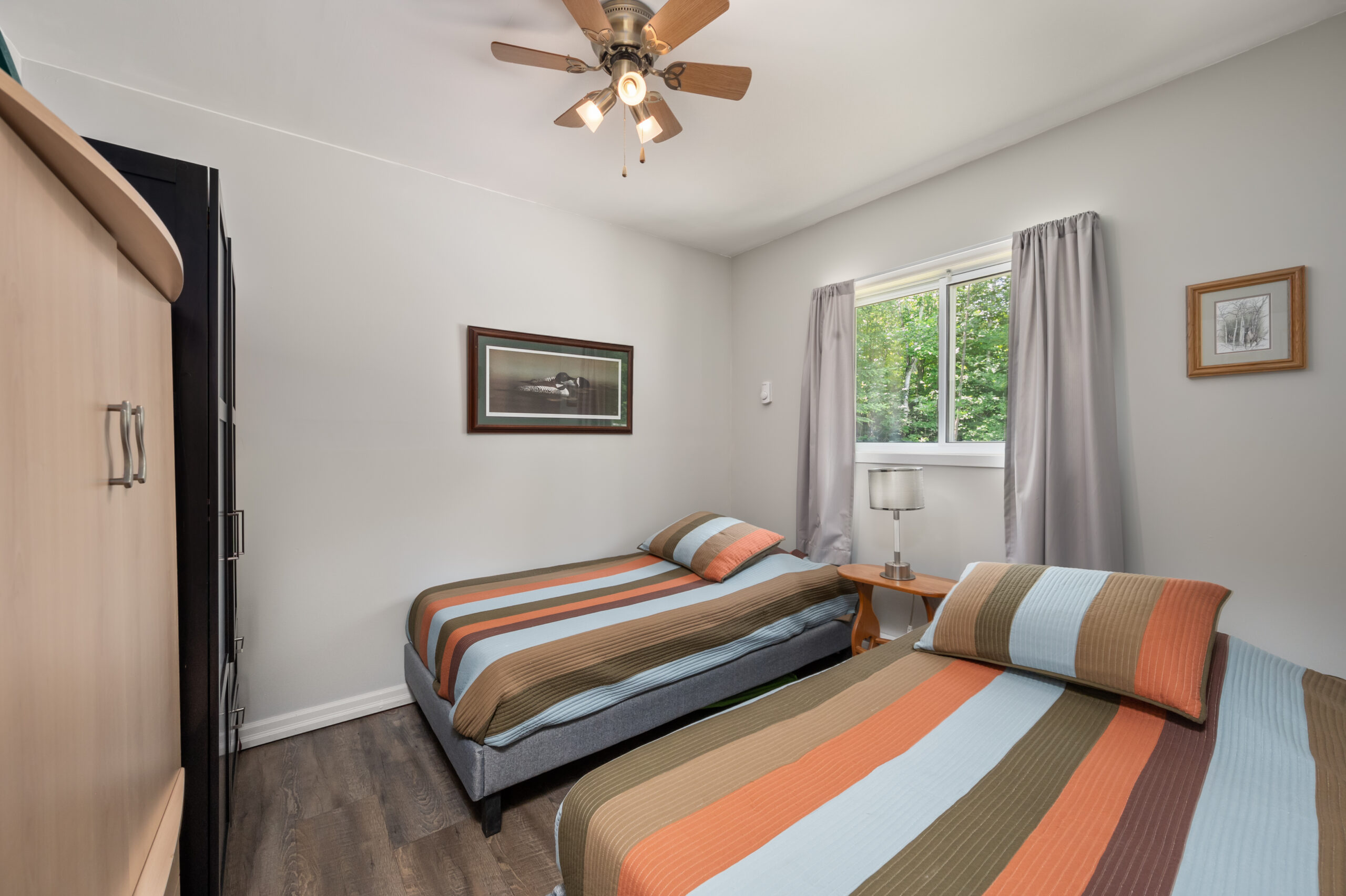 Two twin sized beds with striped covers face away from a wall with a large window