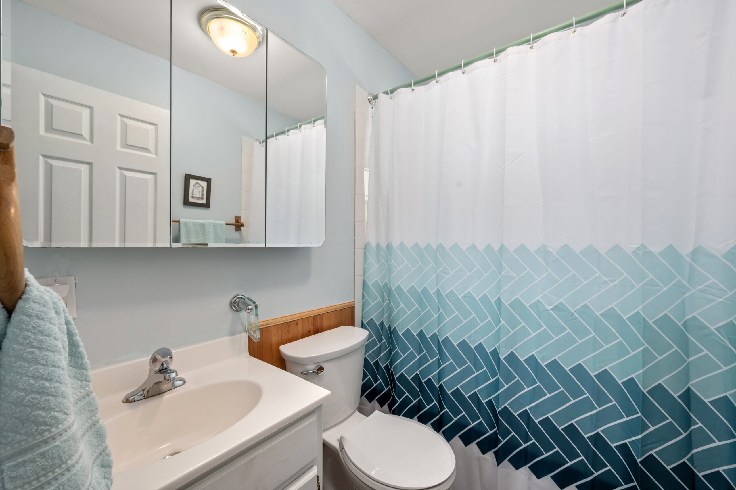 A white sink next to a white toilet. To the right, a closed shower curtain with a white to dark blue vertical gradient