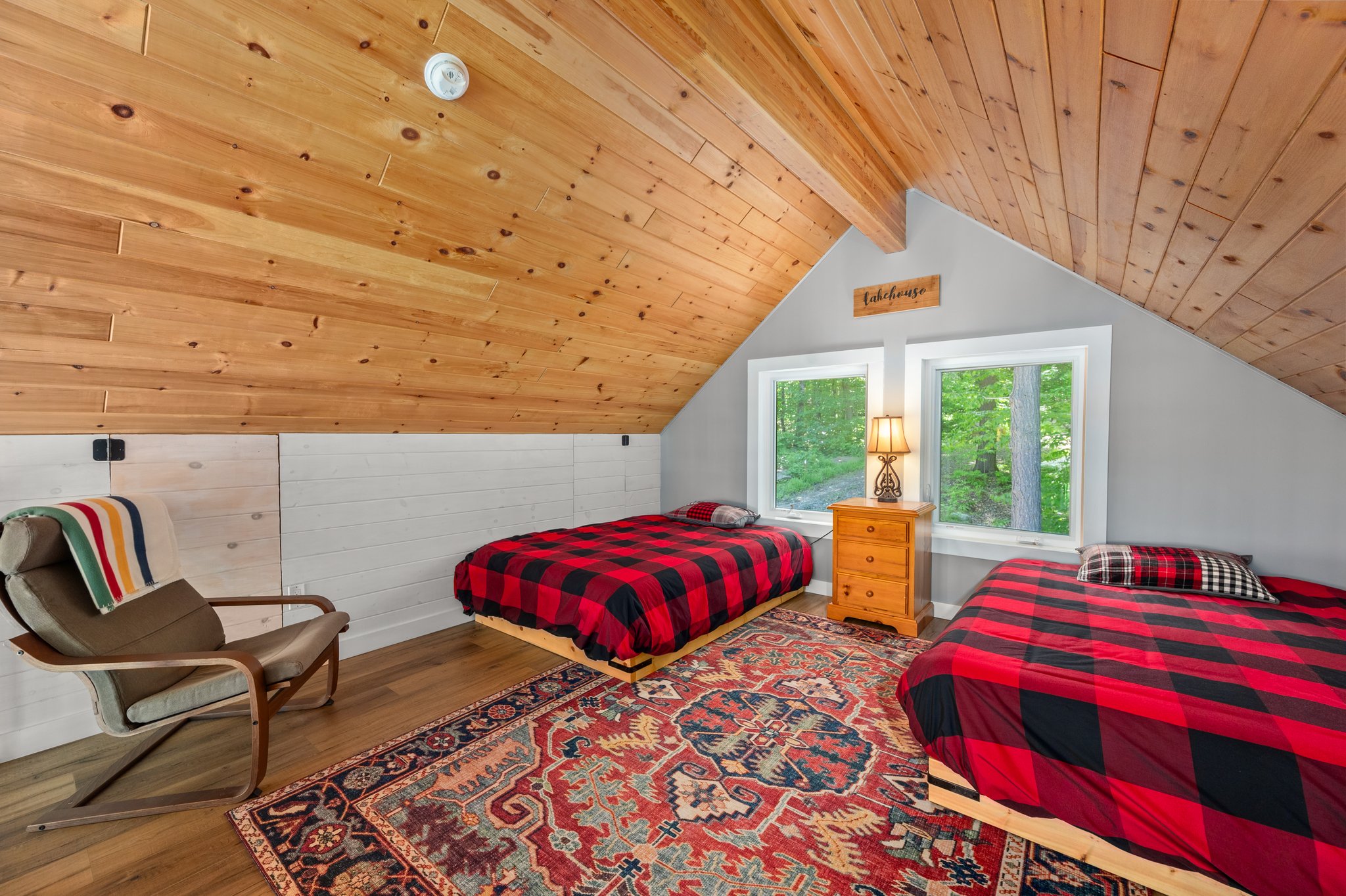 Two beds with red-and-black checked bedspreads in a room with a wood-panelled, V-shaped ceiling
