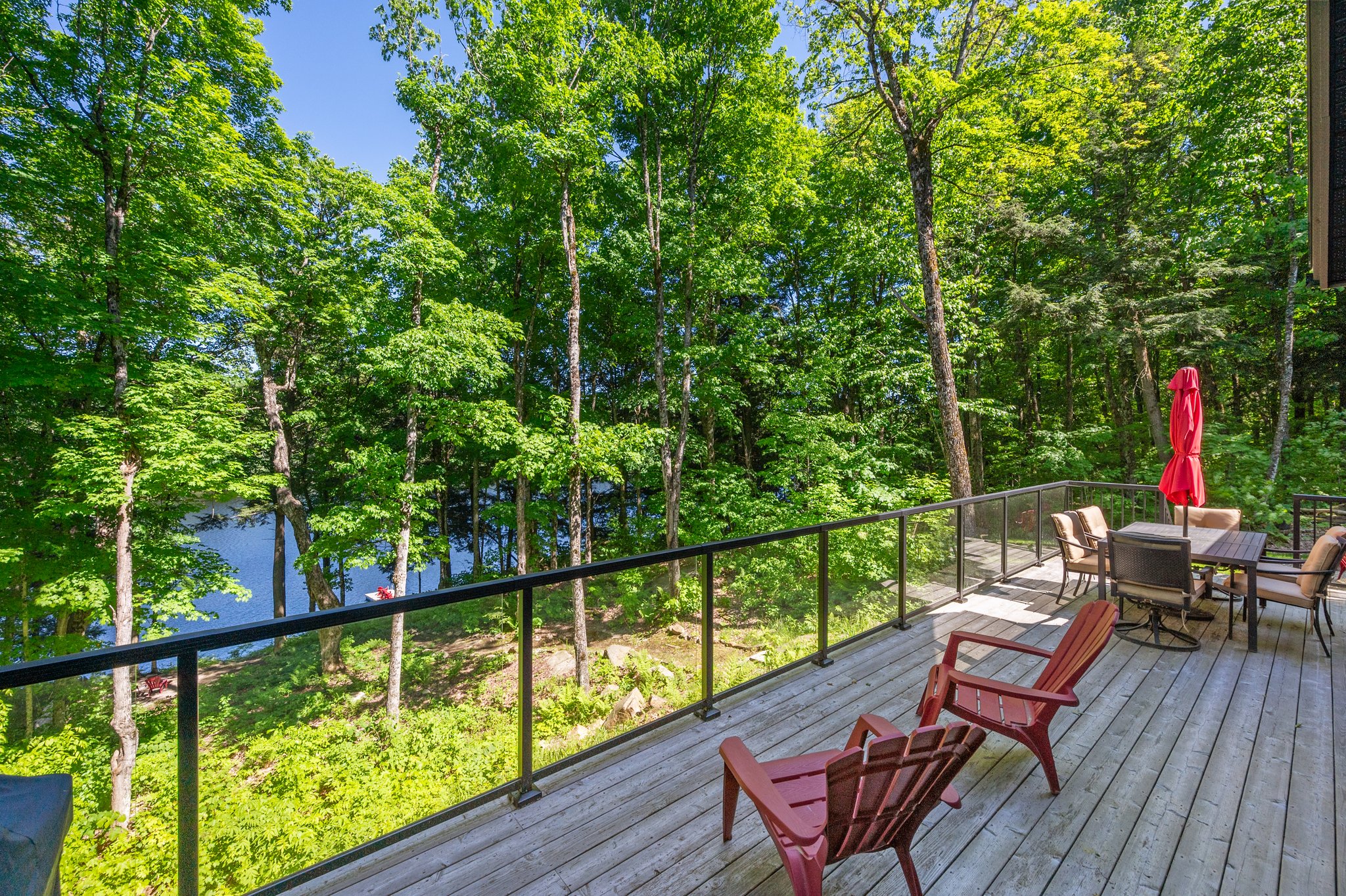 Two red Muskoka chairs face glass railings and the lake