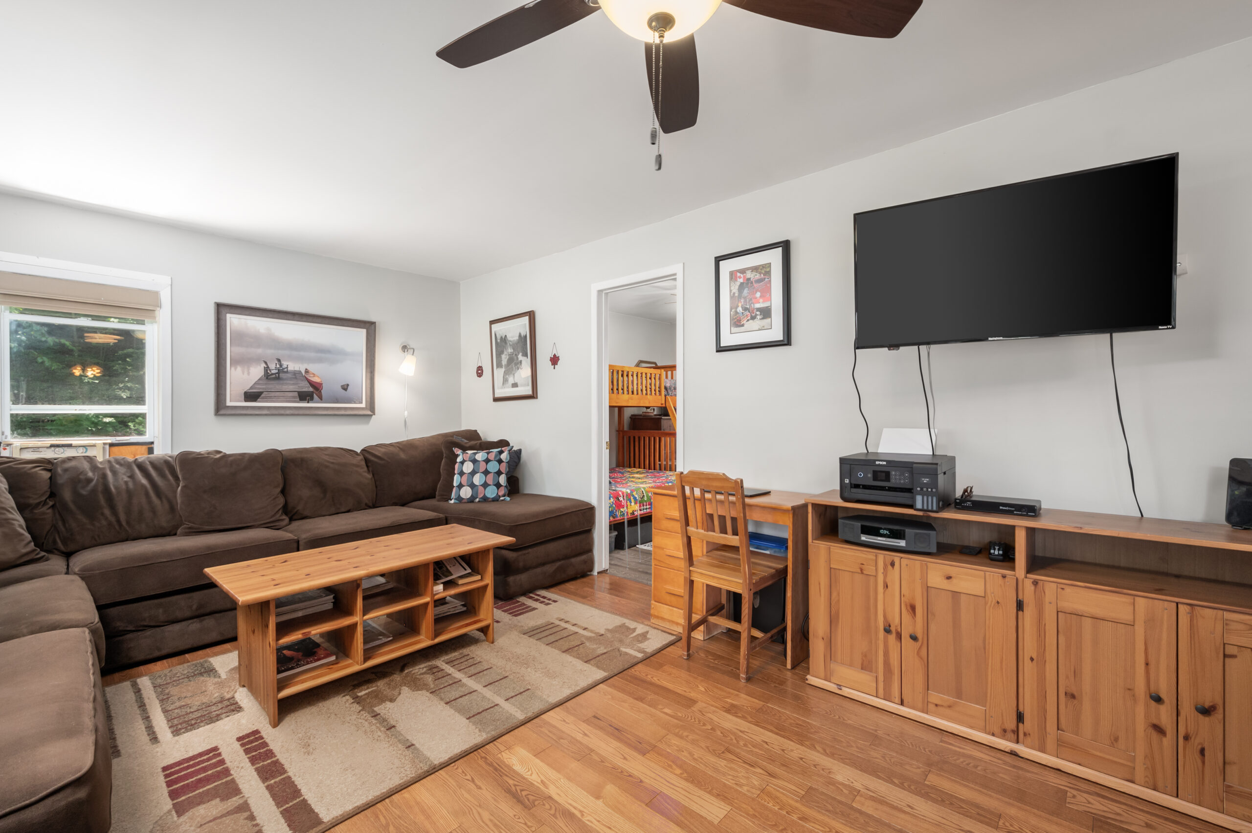 A brown velvet couch behind a wood coffeetable. To the right, a wall with a hanging TV and a dresser