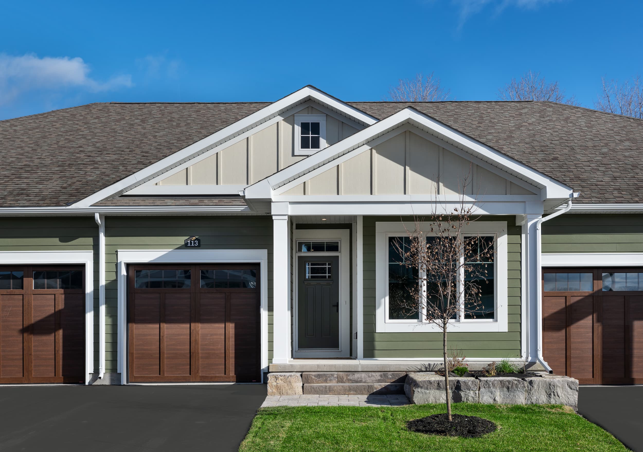 A green panelled home with a brown garage and a manicured green lawn
