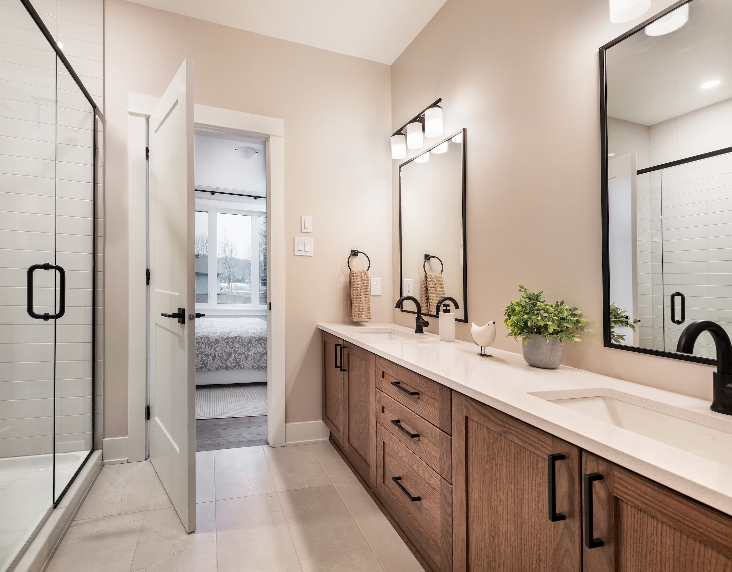 A bathroom door is open. To the left, a glass shower. To the right, a long vanity with a double-sink and two mirrors